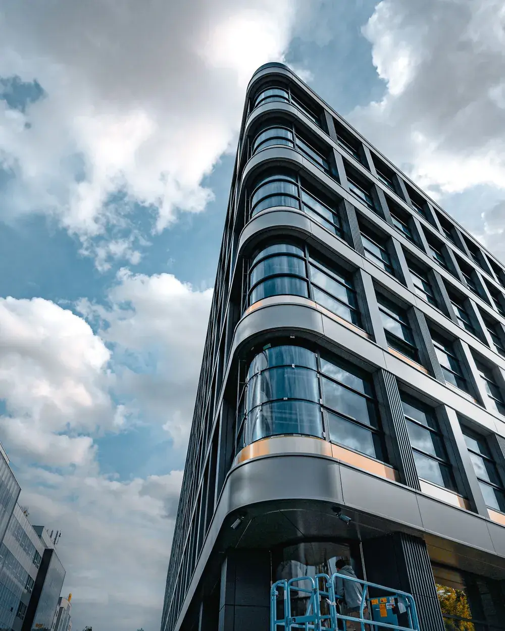 A modern glass office building rising against a cloudy blue sky.