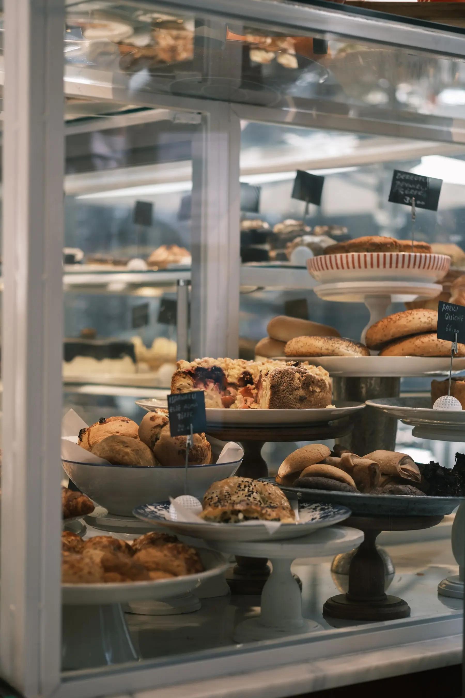Tarts and pastries arranged on stands in a glass cabinet.
