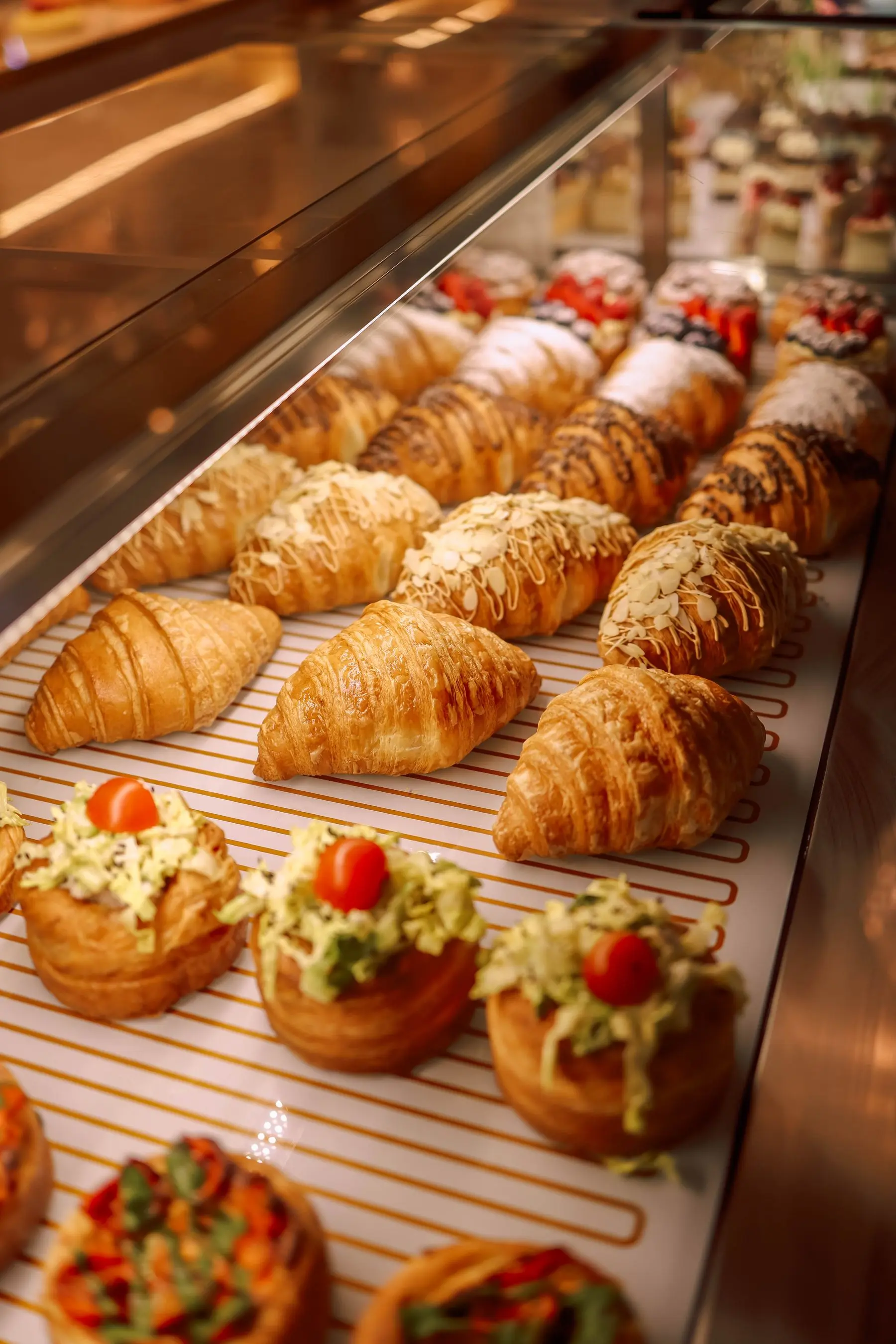 A glass display case of croissants and savoury pastries, lit warmly.
