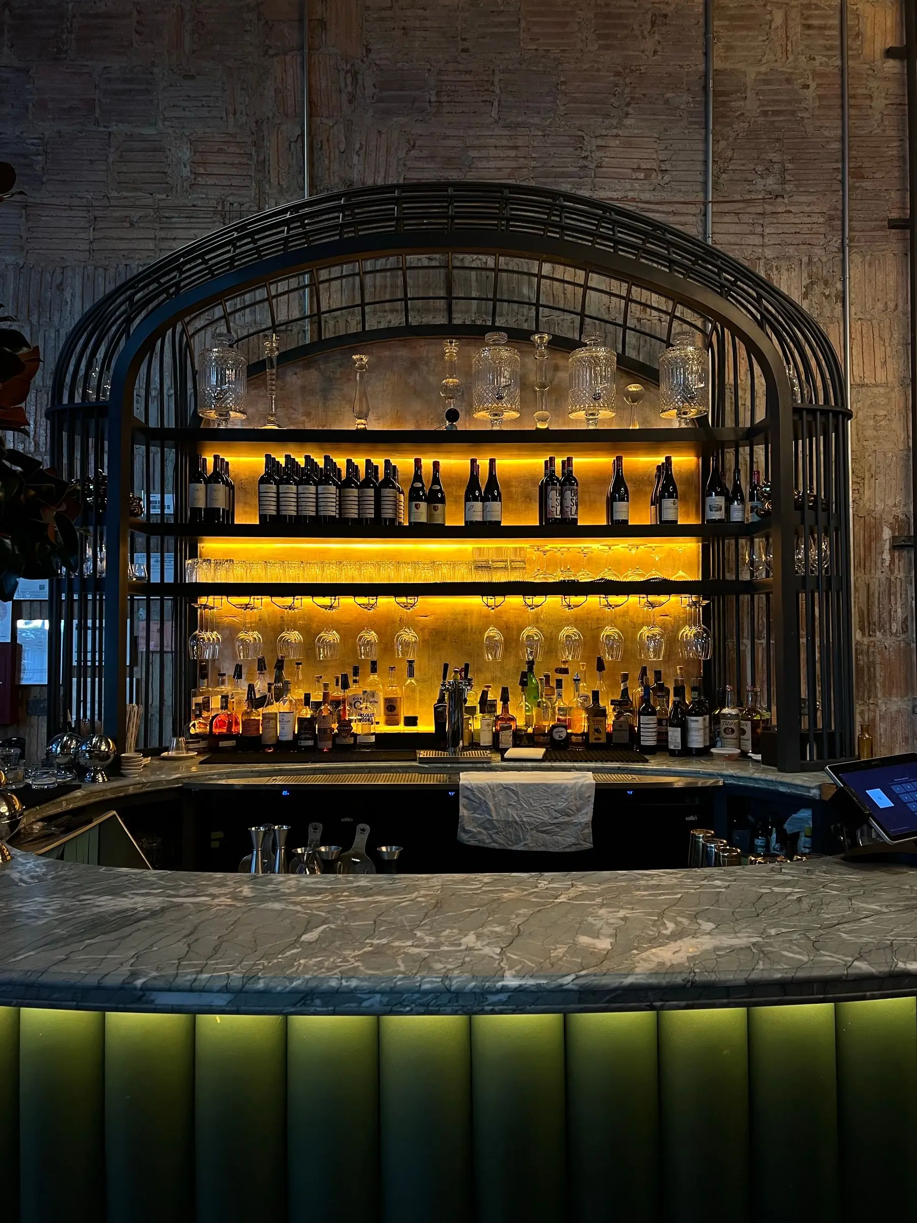 An arched iron frame holds bottles and glasses above a round marble bar, lit amber.