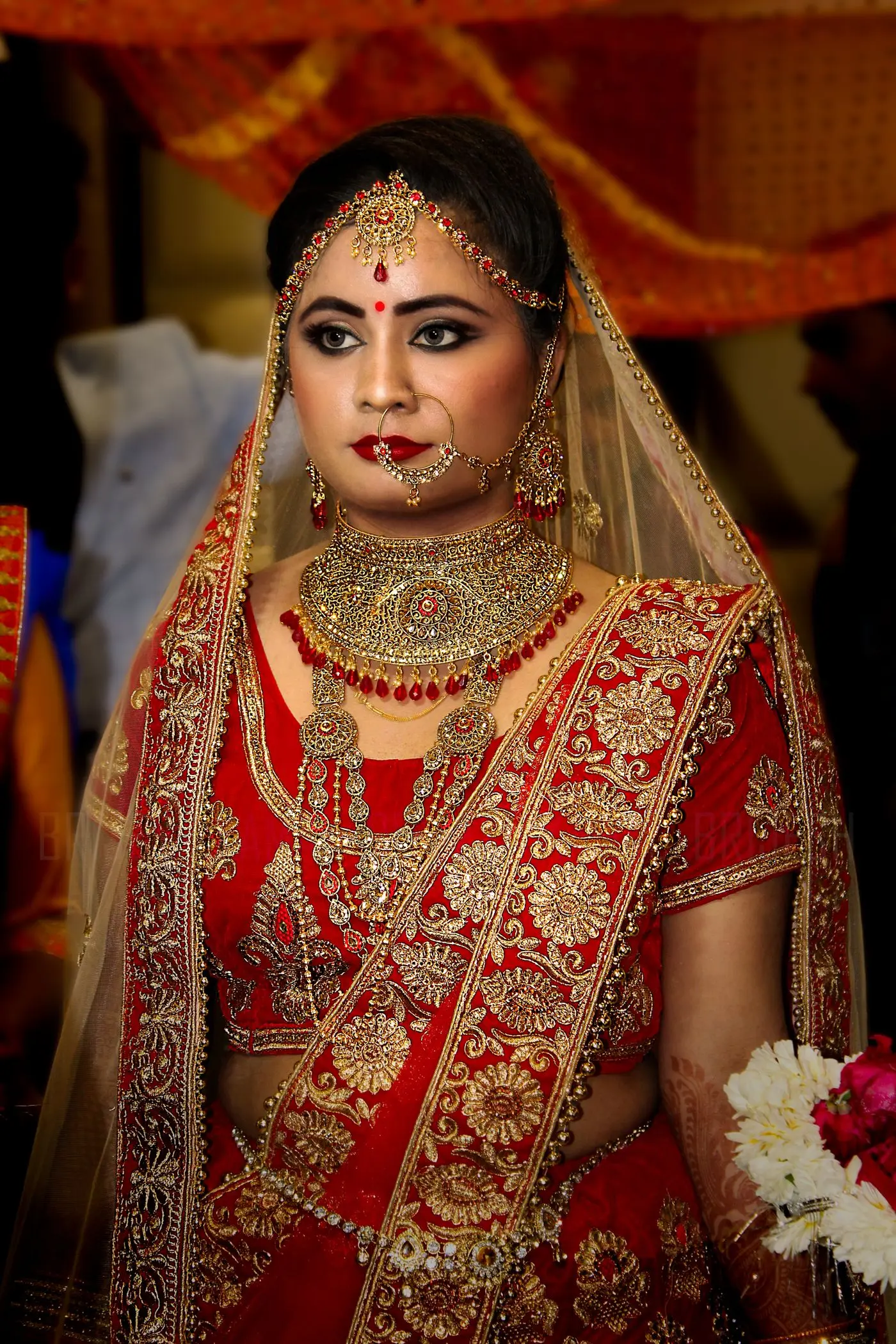 A bride in red and gold, wearing a heavy gold necklace, earrings and a nose ring.