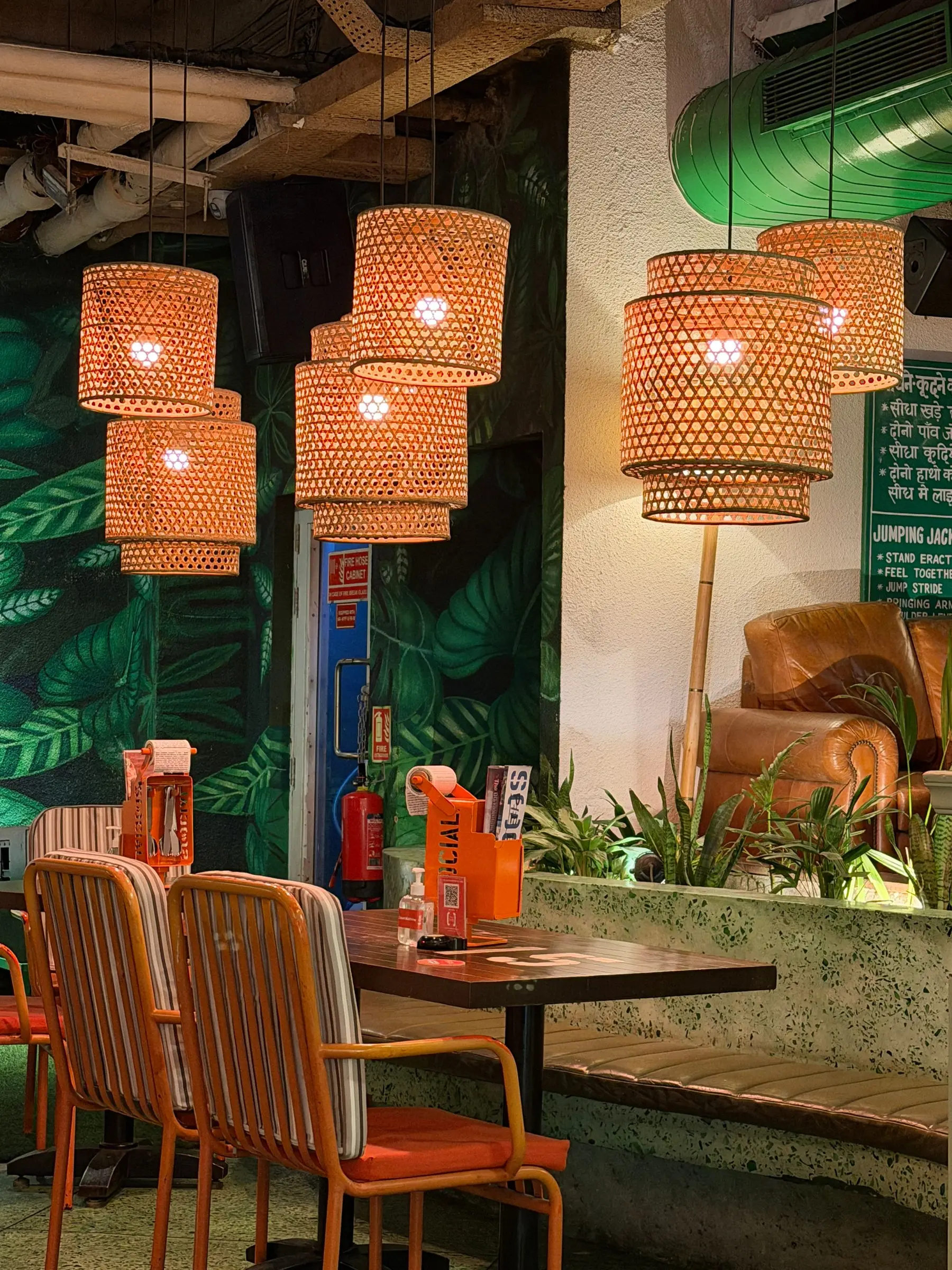 Woven rattan pendant lamps glowing orange against a wall of tropical leaves.
