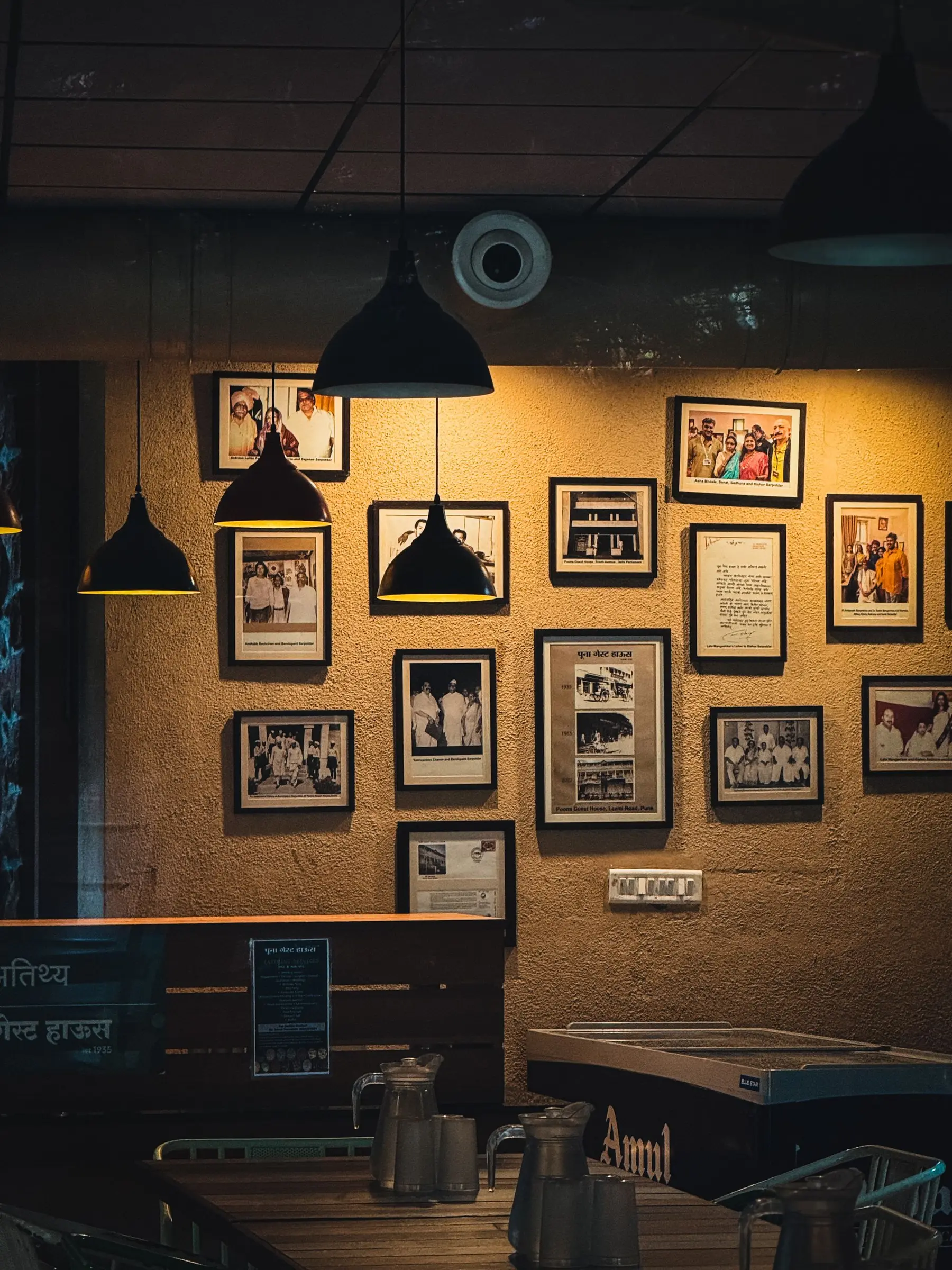 A wall of framed black-and-white photographs lit by two black pendant lamps.