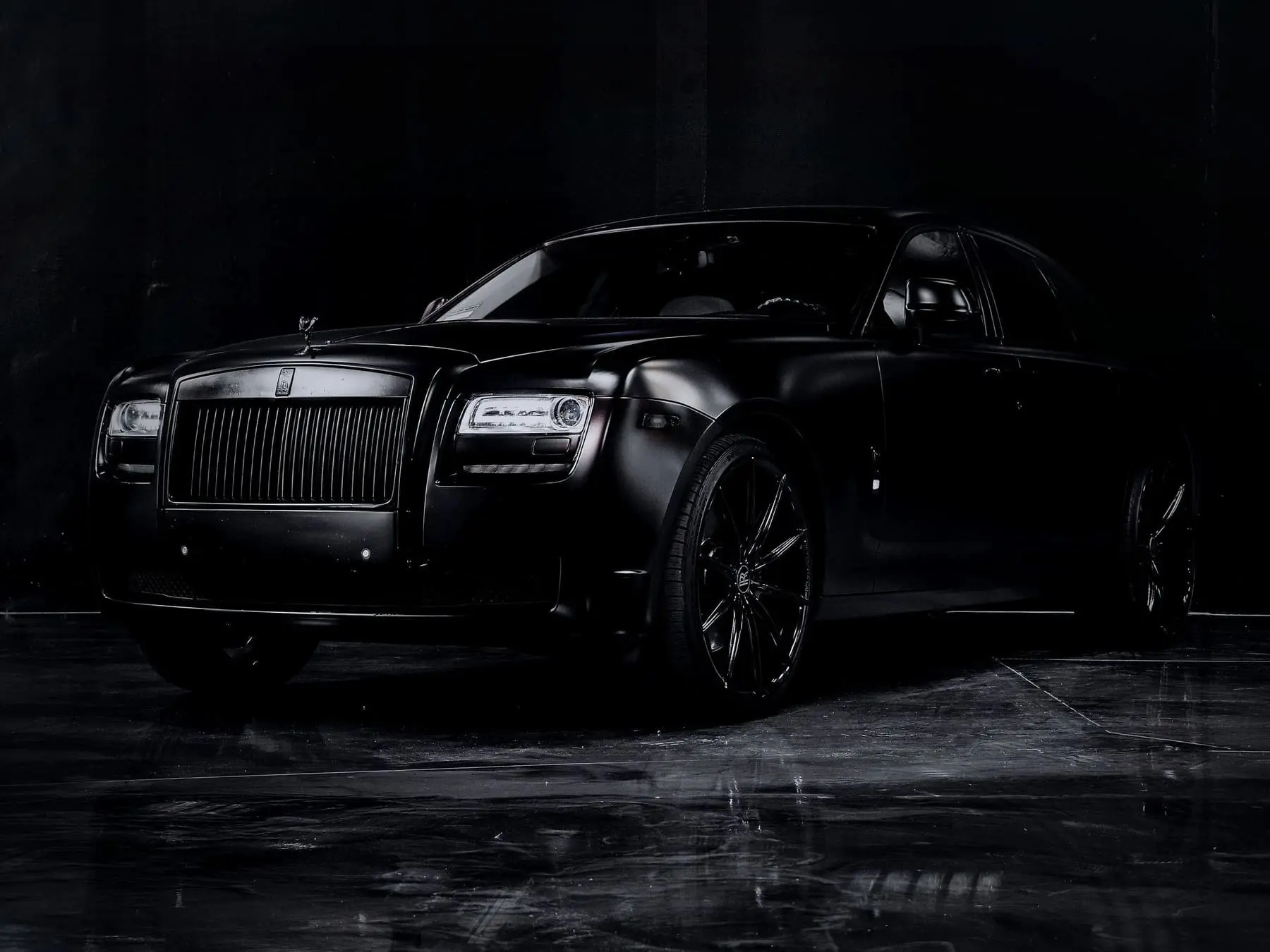 A black saloon, three-quarter front, picked out of the dark by one soft light.