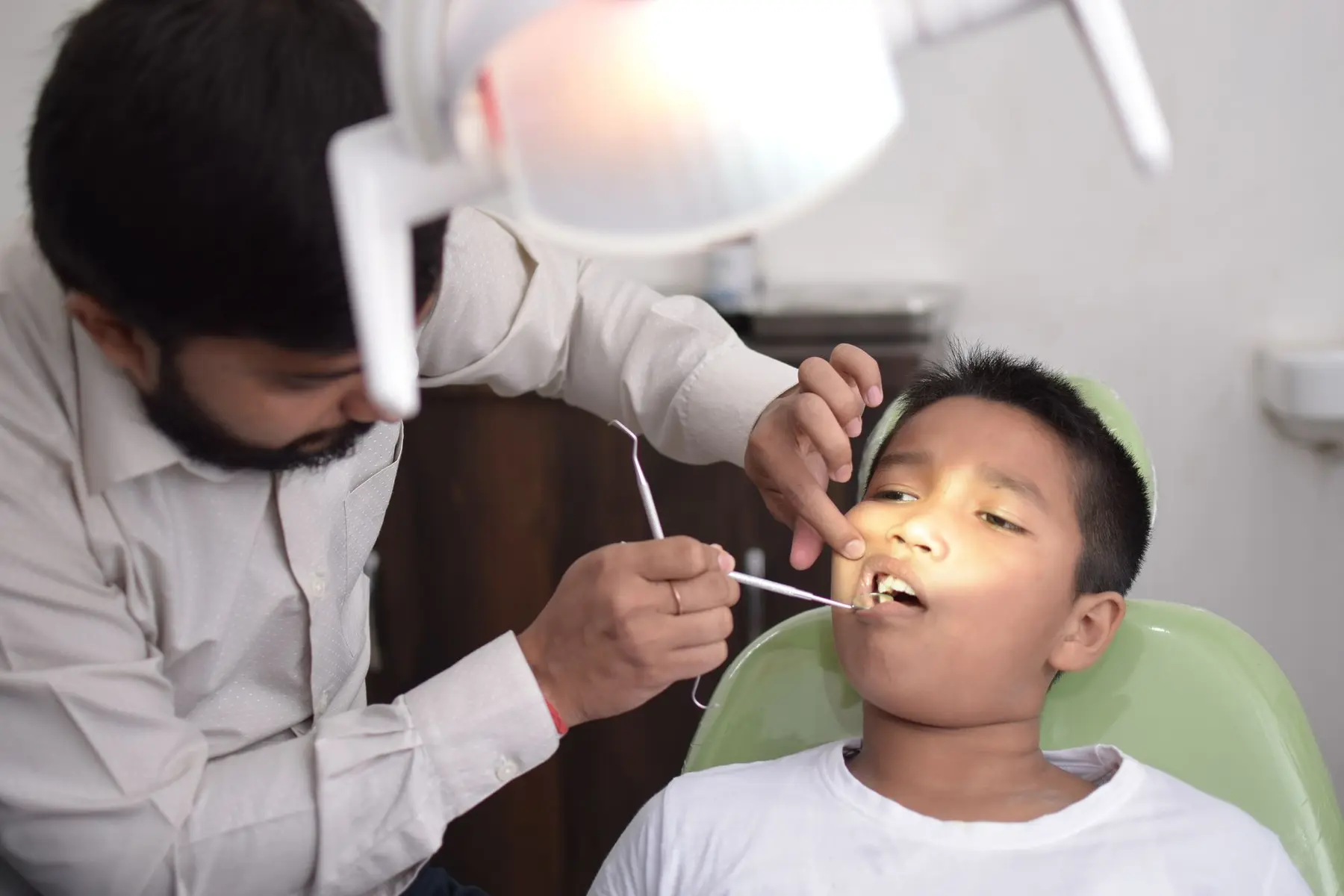 A dentist examining a young patient who is smiling in the chair.