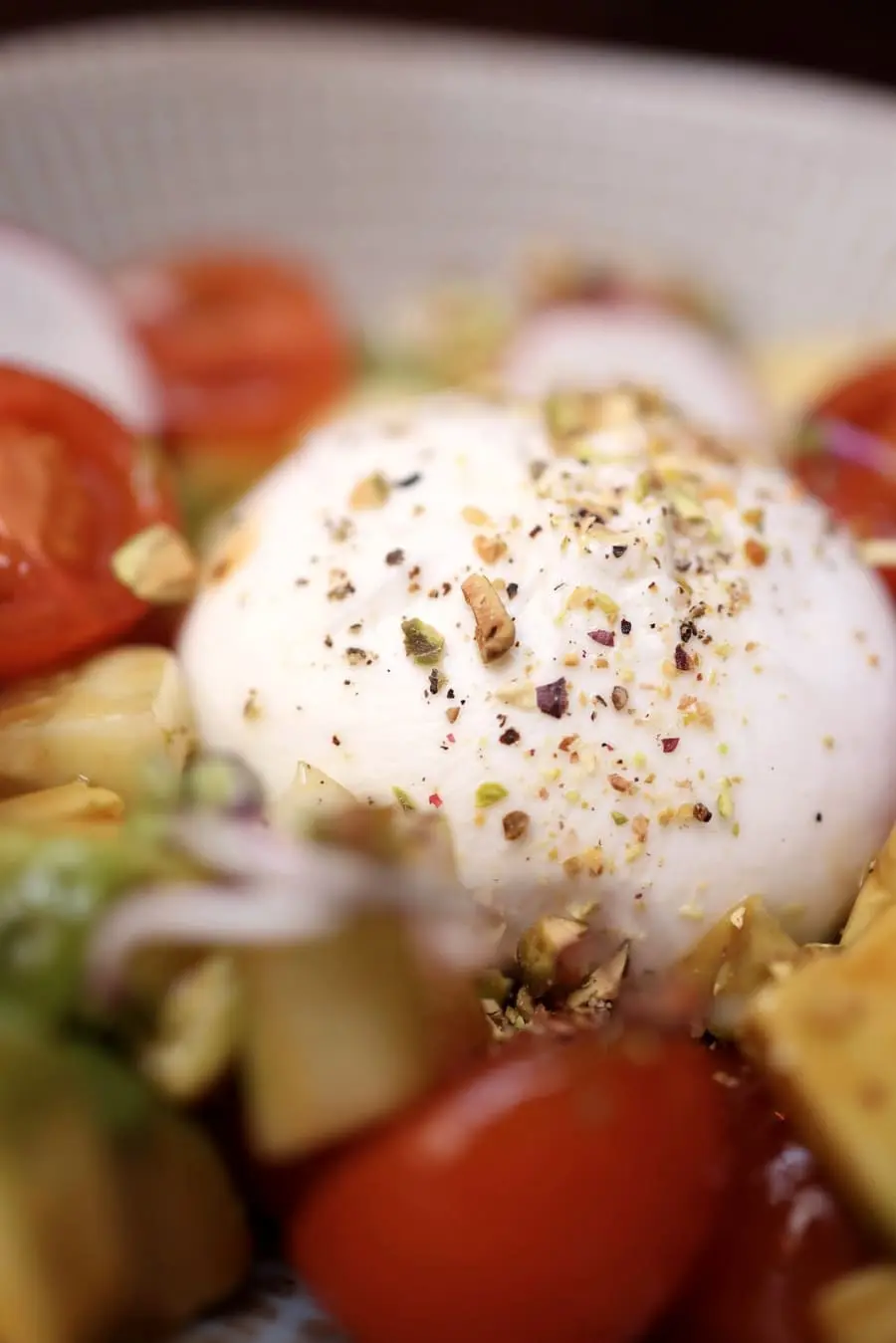 A whole burrata scattered with crushed pistachio among cherry tomatoes.