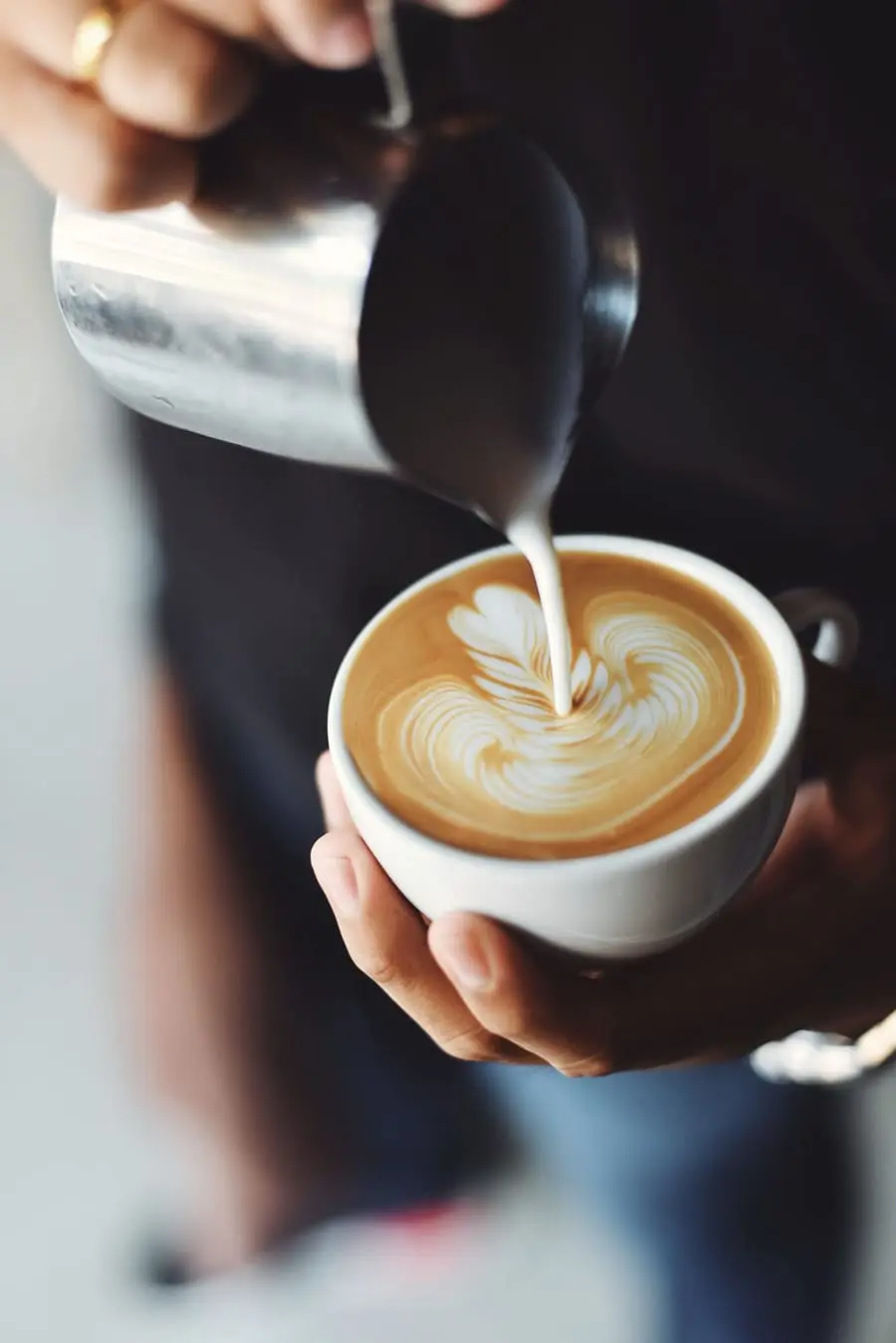 A barista pouring steamed milk into a white cup.