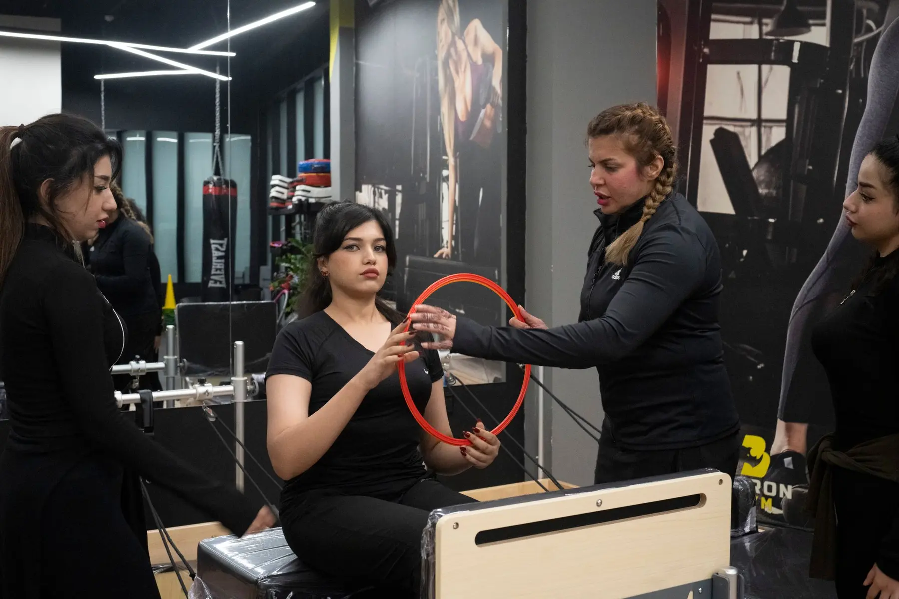 A coach guides a client through a reformer pilates exercise with a ring.