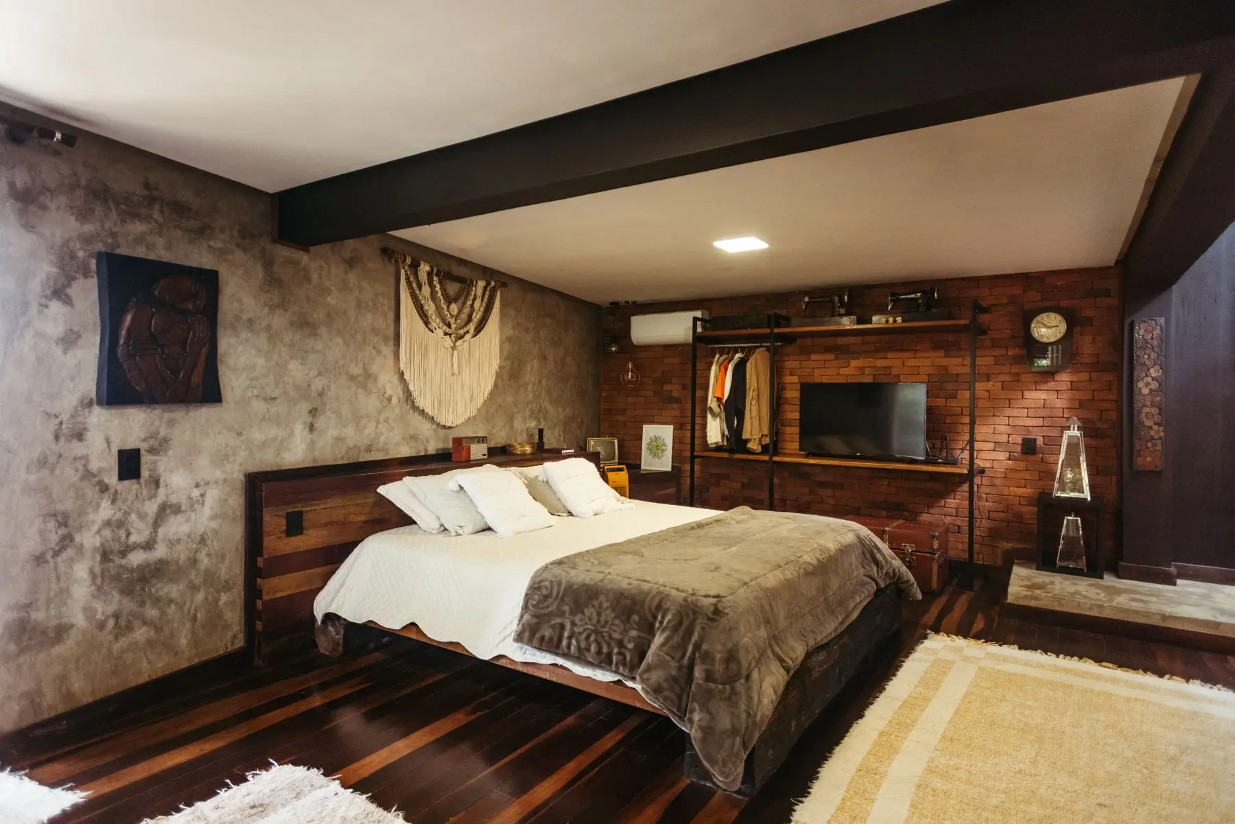 A bedroom with a wooden bed, brick wall and woven hanging, lit softly.