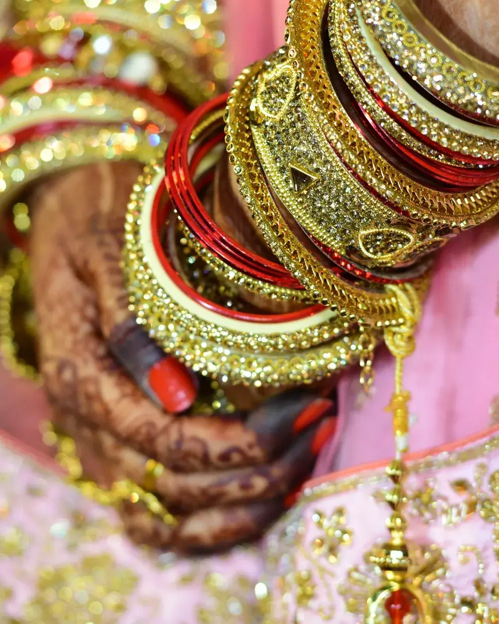 A hand with fine henna patterns wearing a stack of gold, green and red bangles.
