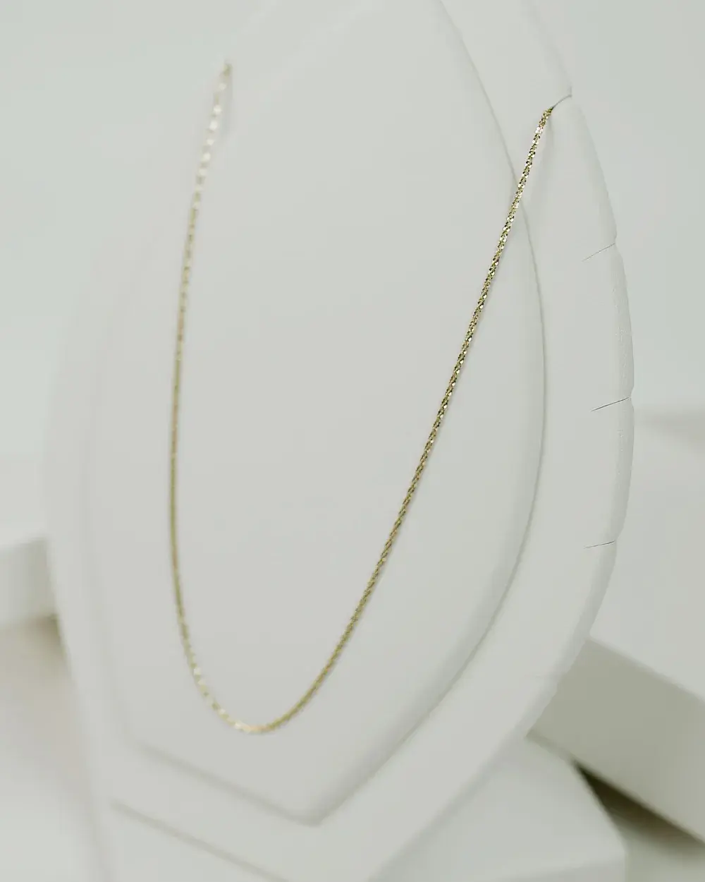A single fine gold chain laid along a pale display bust.