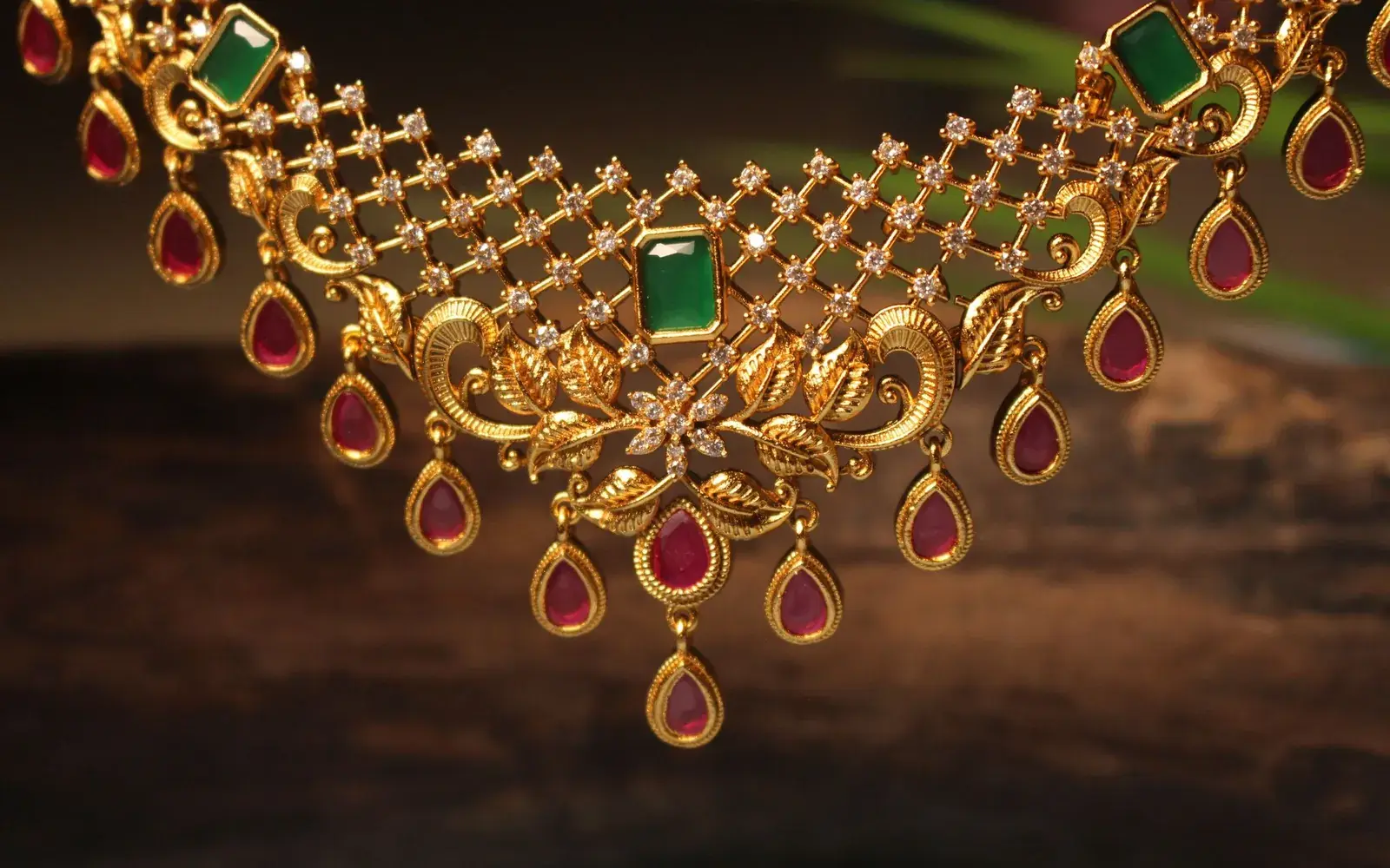A gold collar necklace set with rubies and an emerald, lit warmly against a dark ground.