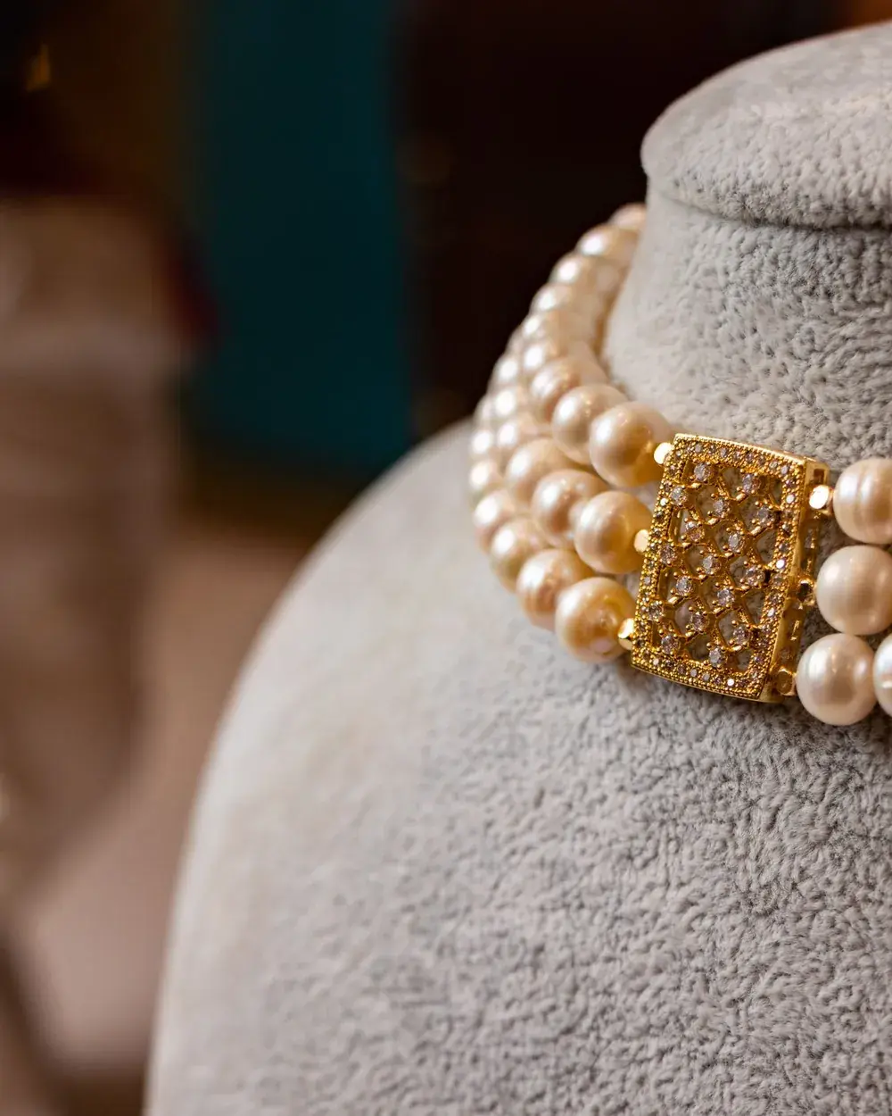 A three-strand pearl choker with a gold clasp on a grey velvet bust.