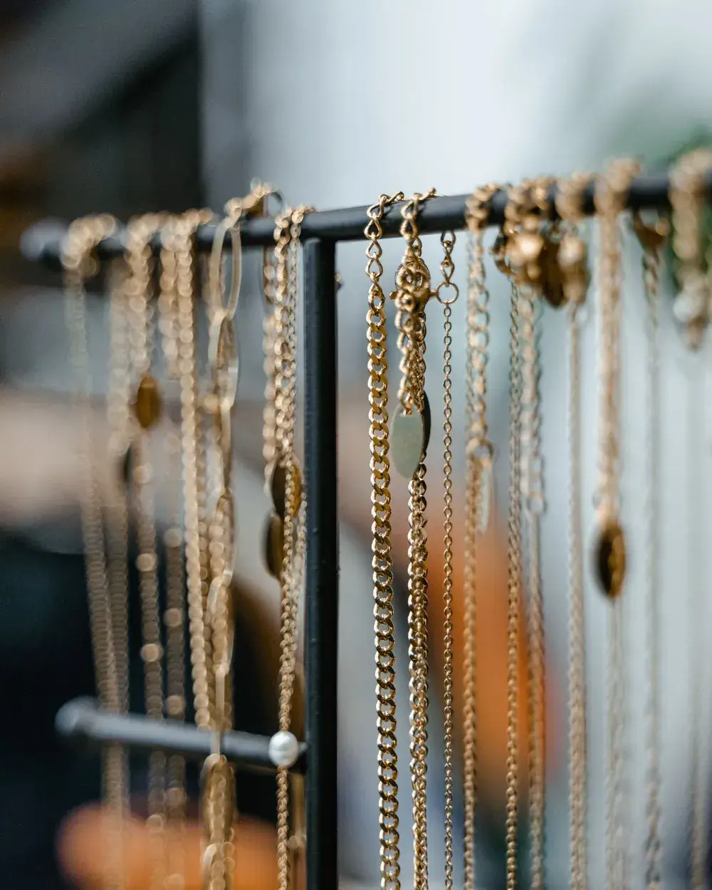 Fine gold chains and pendants hanging from a black display stand.