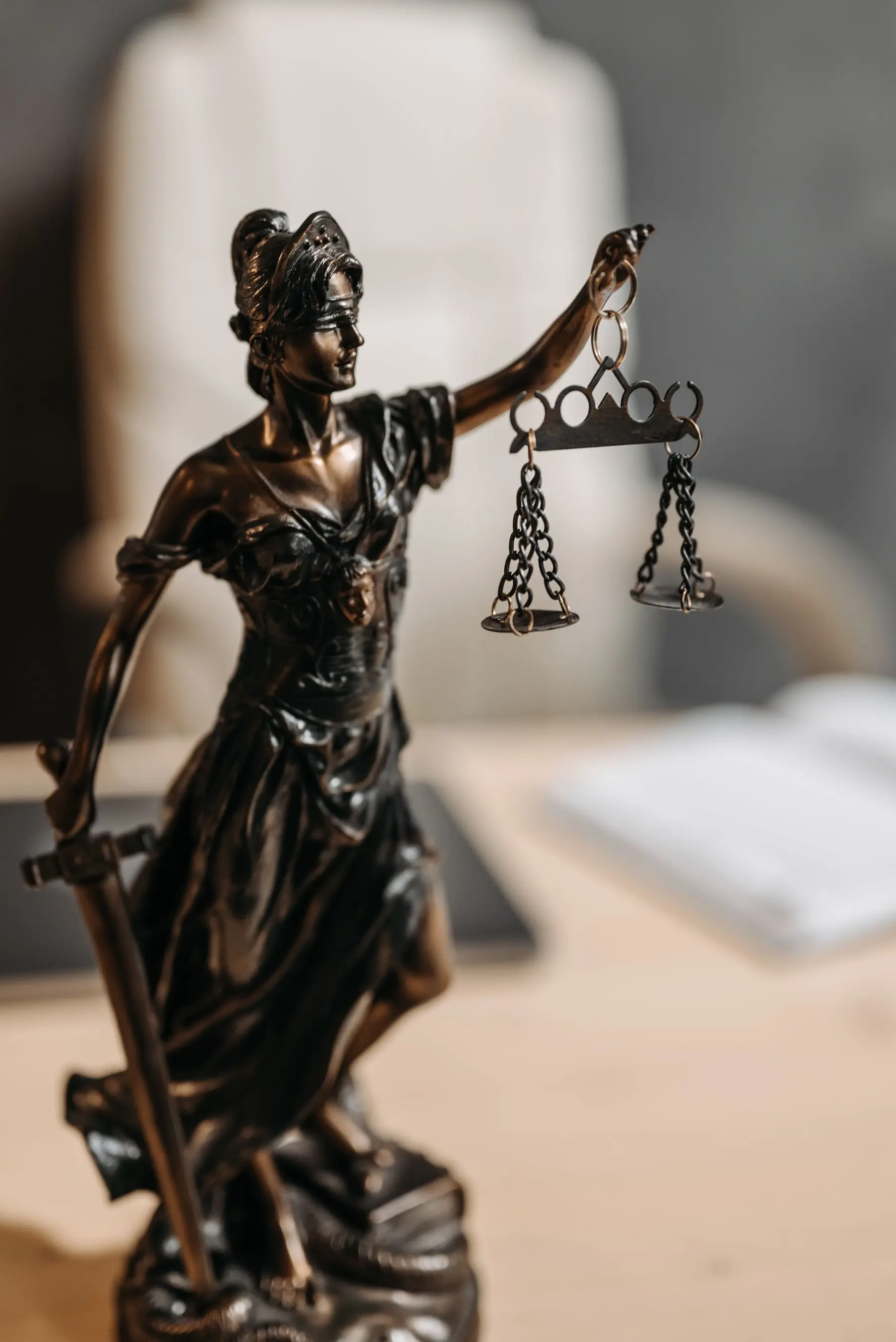A bronze Lady Justice raises her scales against a softly blurred desk.