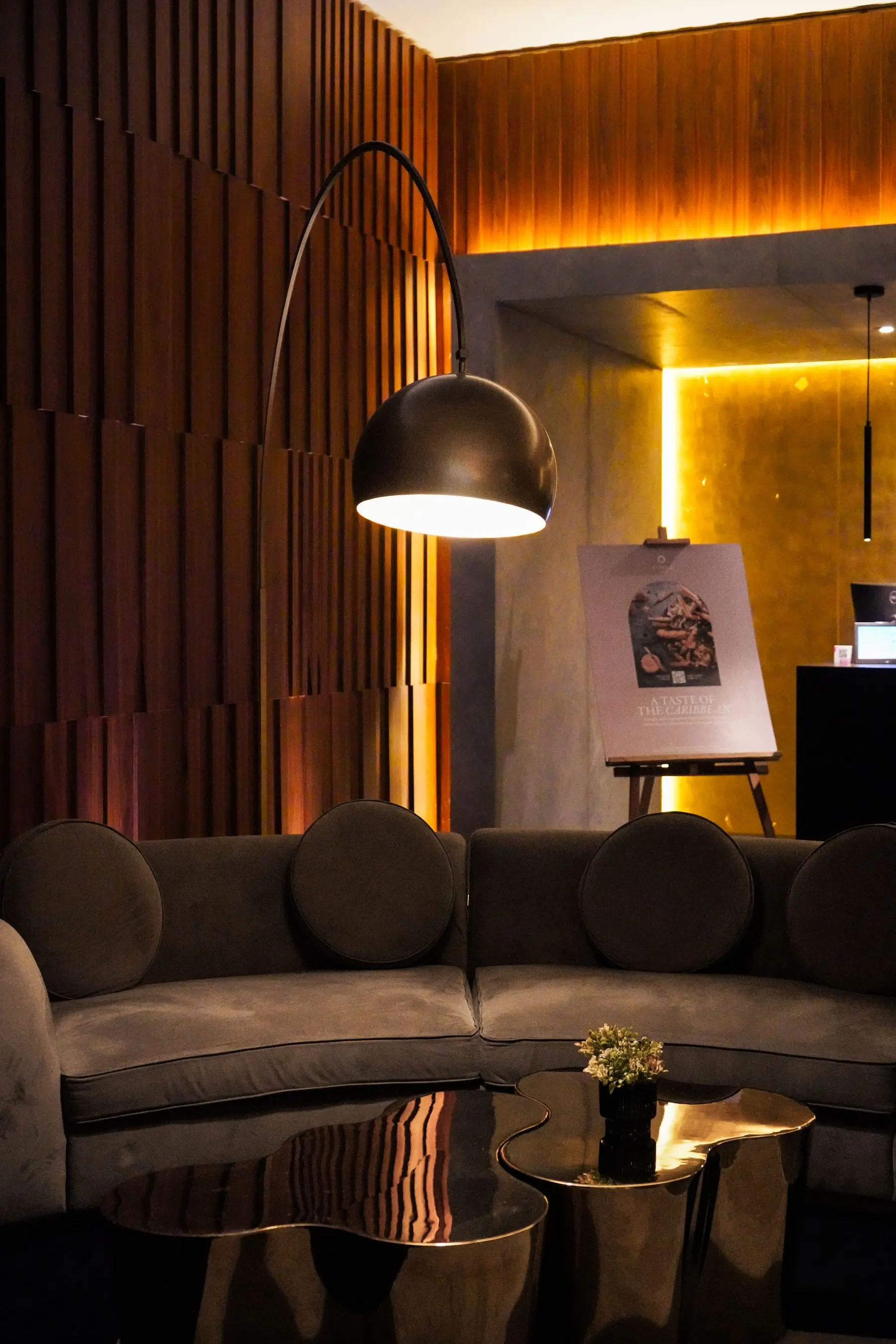 A curved velvet sofa beneath an arched lamp, with a gold-lit wall behind.