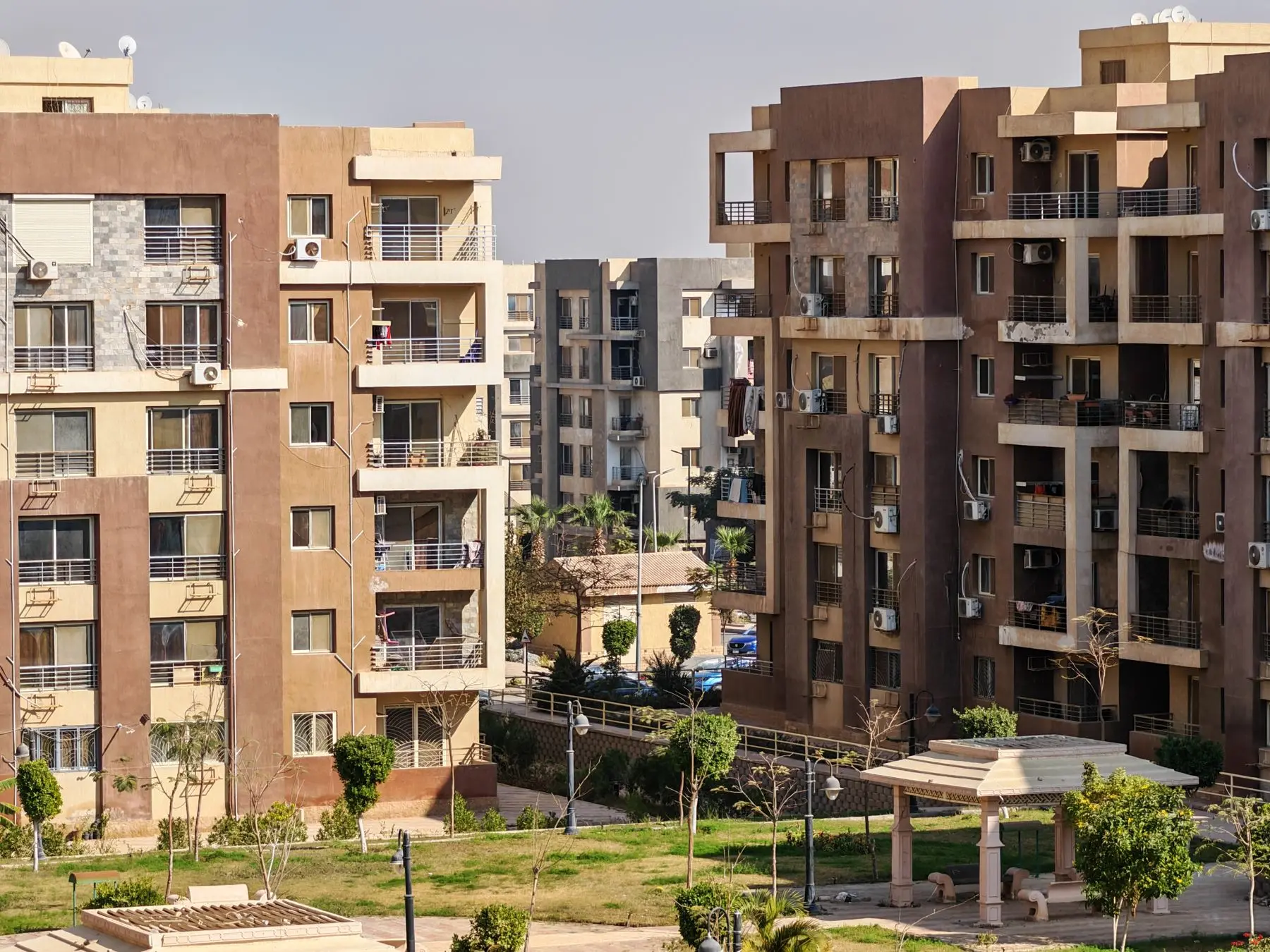 A cluster of mid-rise apartment blocks with balconies around a green lawn in warm afternoon light.