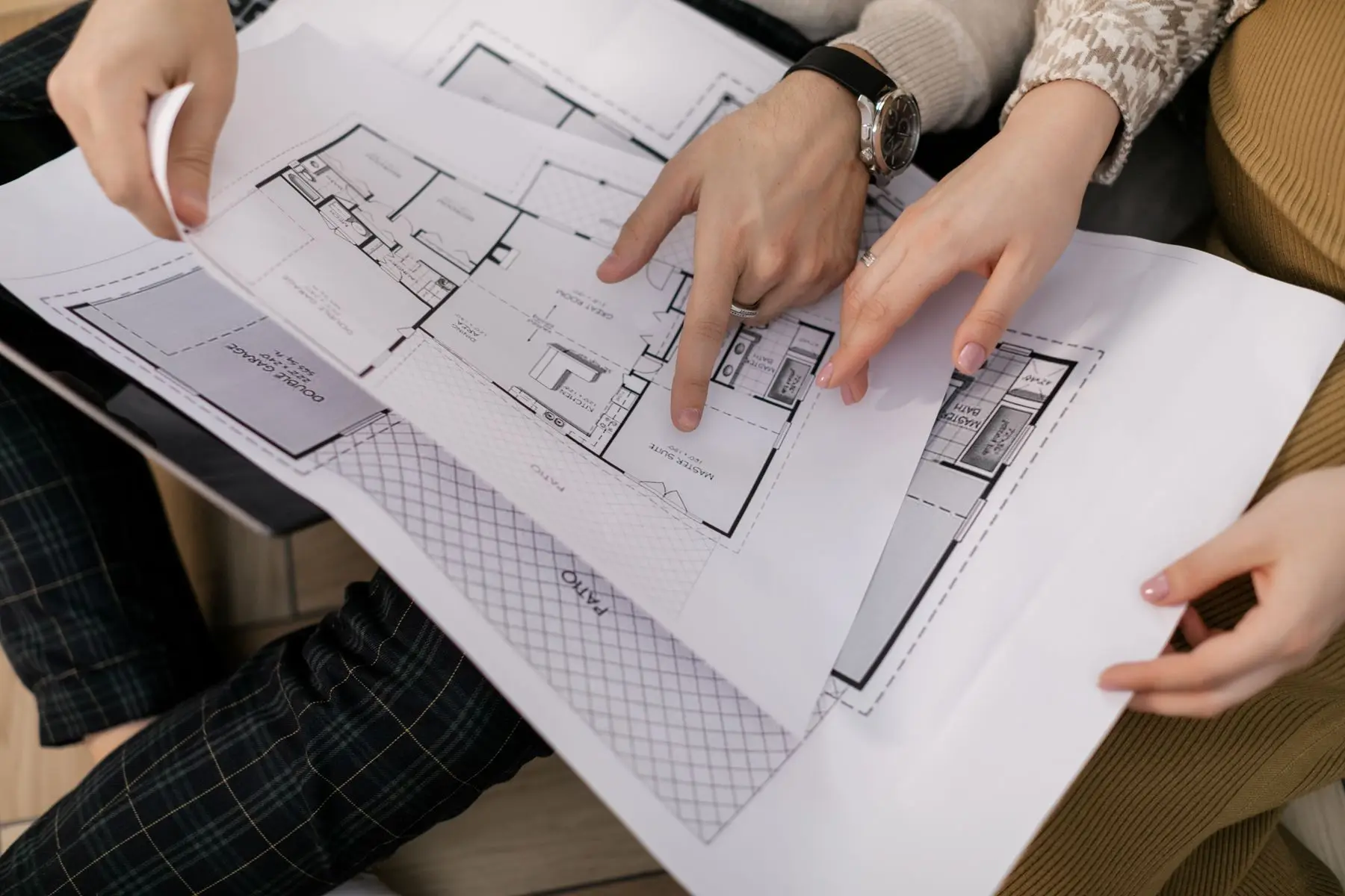 Two people point at floor plans spread across a table.