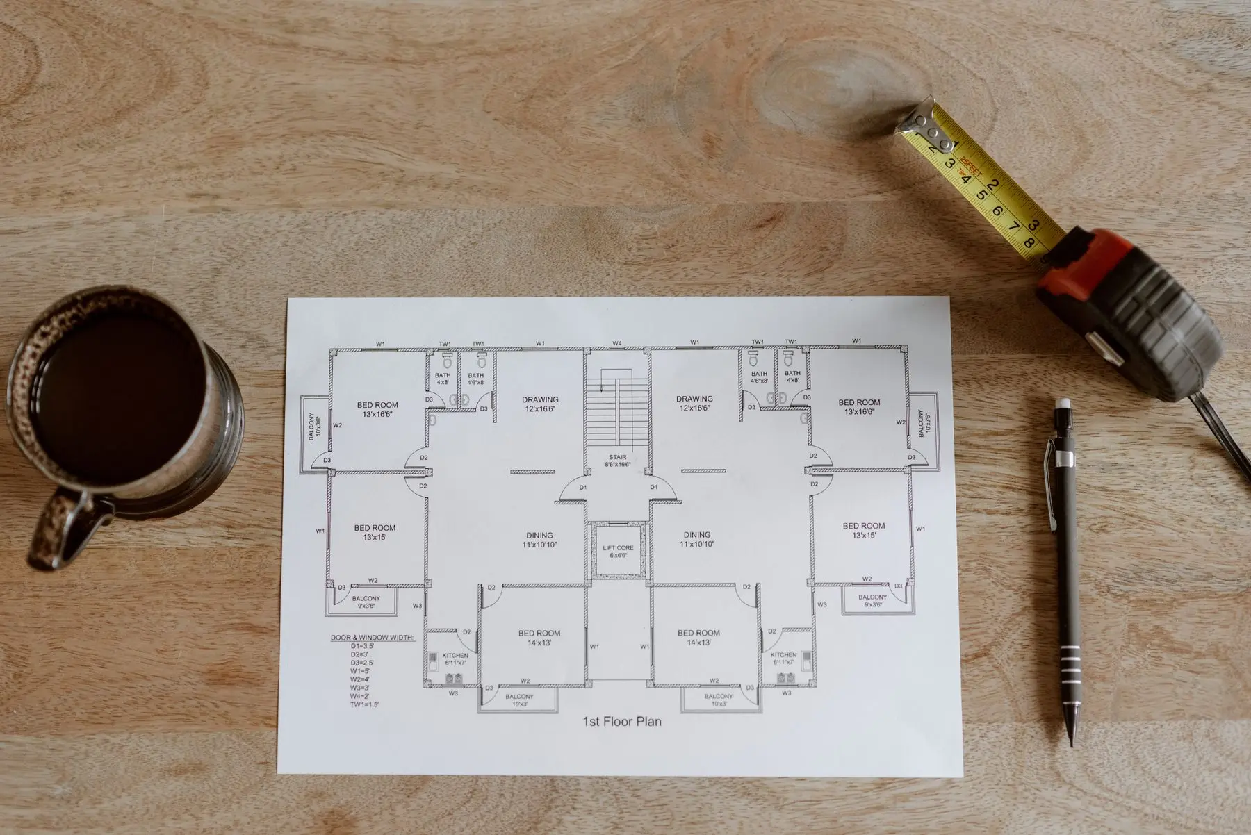 A printed floor plan of a house on a wooden desk, with a tape measure at its corner.