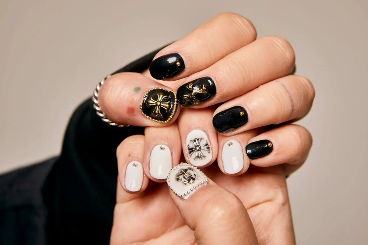 Hands with black and cream nail art, a ring on one finger.