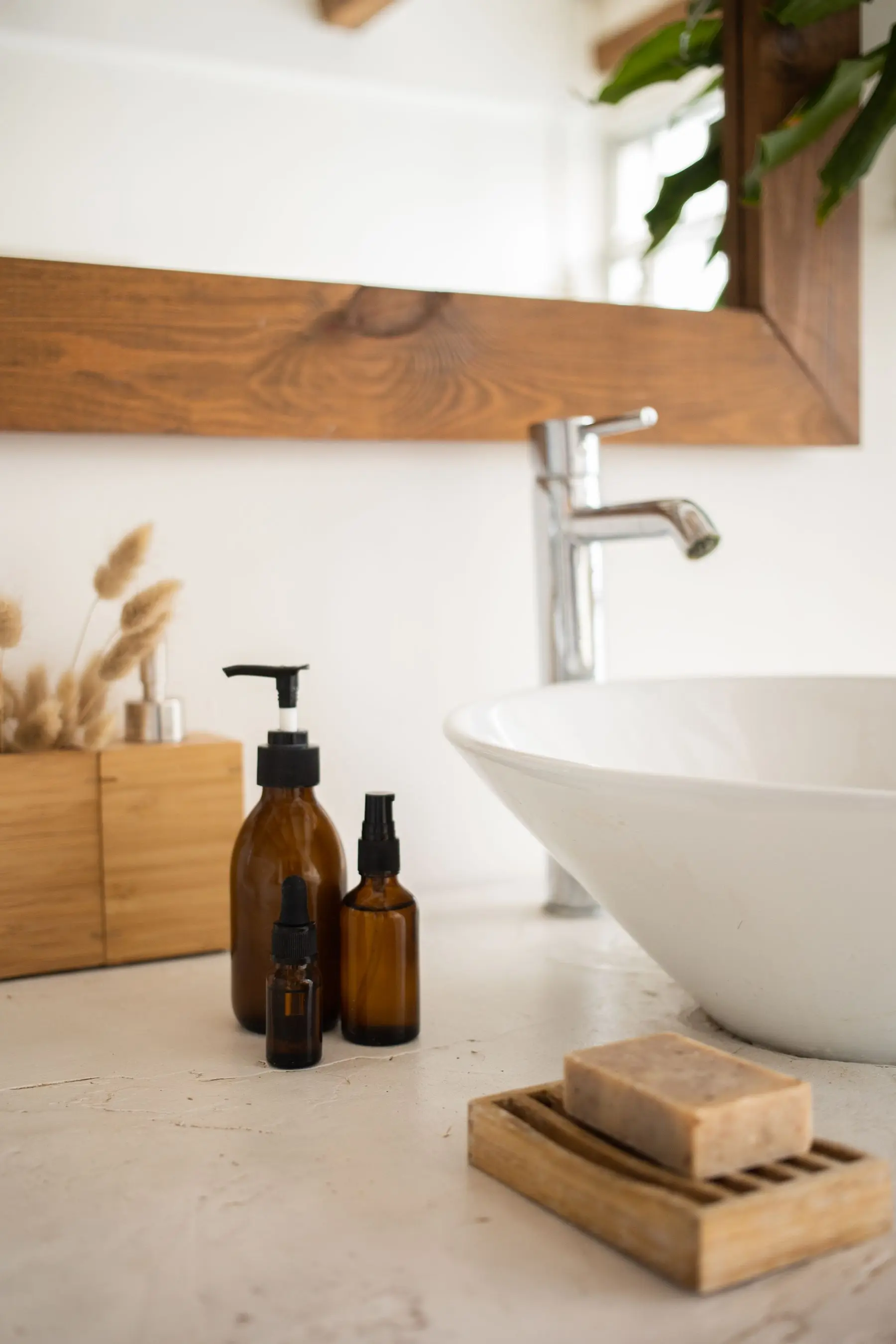 A white basin with amber bottles, a wooden-framed mirror and dried grasses.