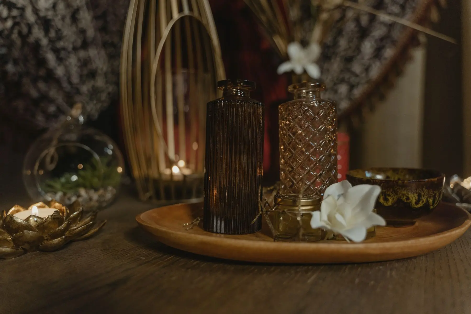 Amber glass bottles and a white flower on a wooden tray, lit by candles.