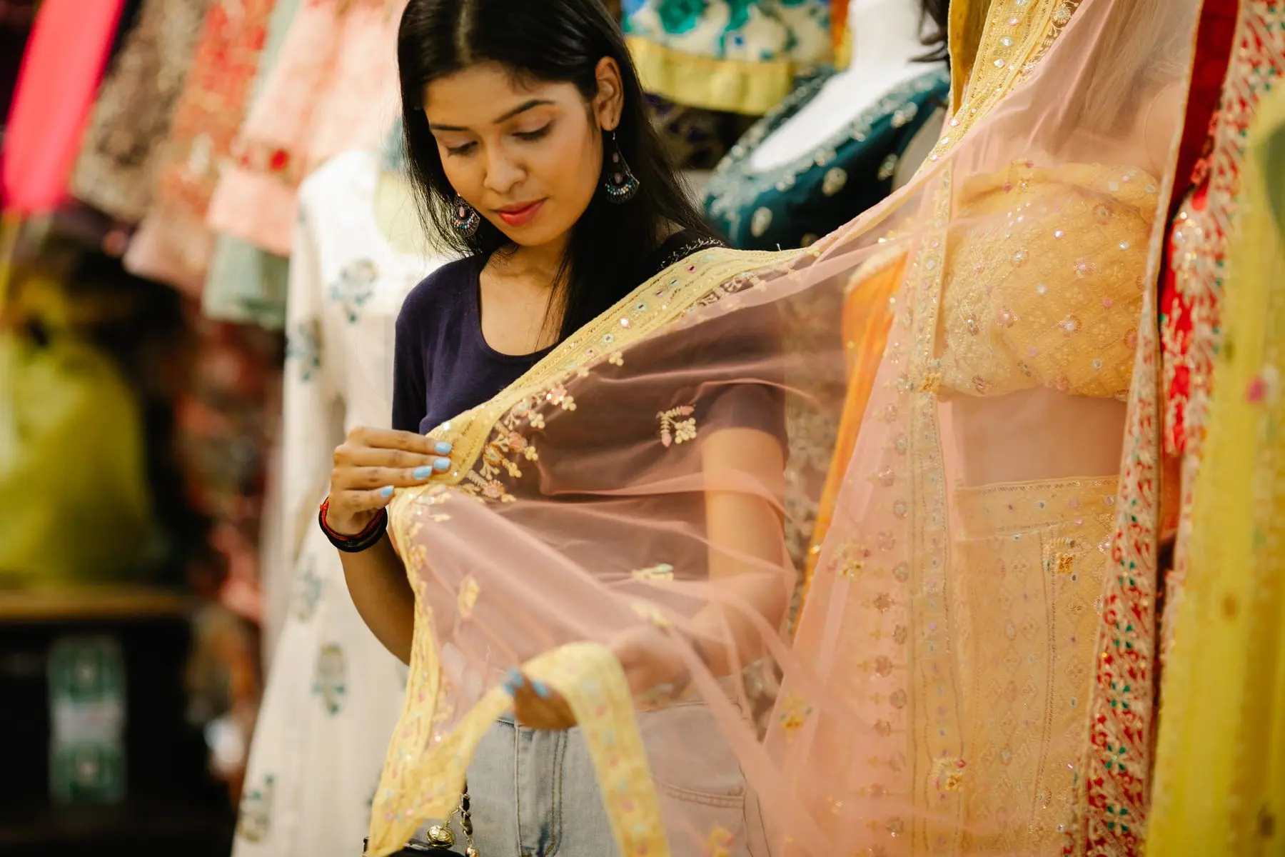 A woman in a shop examines a sheer, embroidered dupatta held up to the light.
