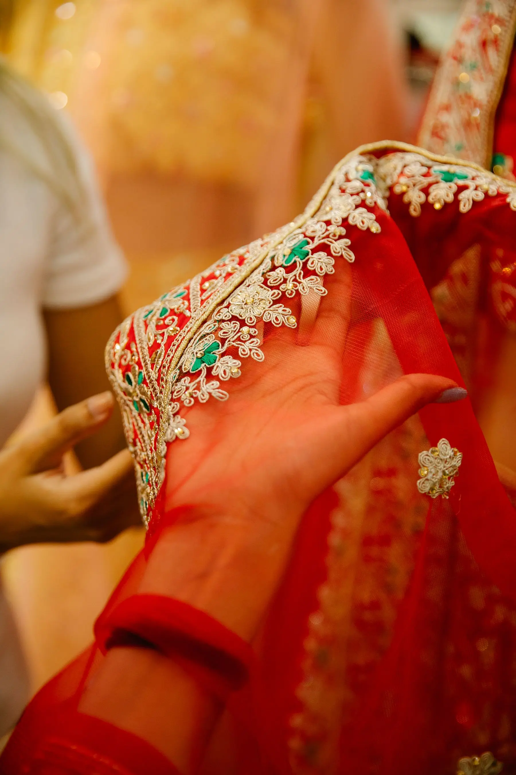 A hand holds a piece of red fabric with delicate gold embroidery.