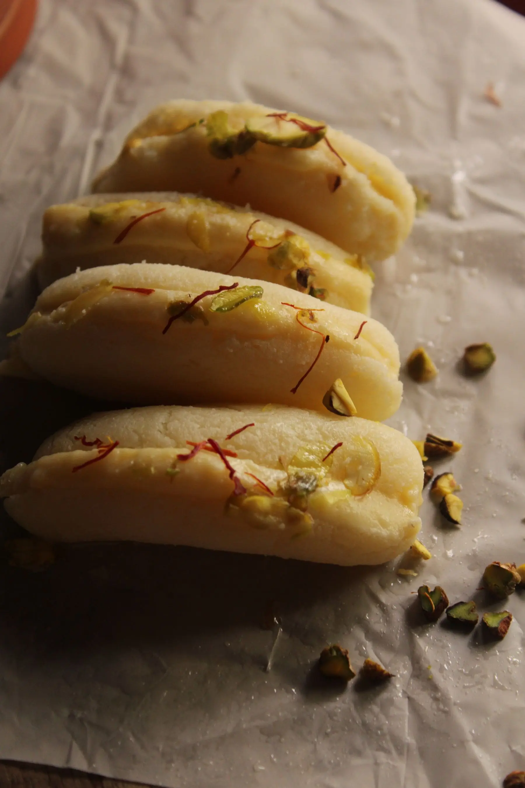Stuffed milk sweets topped with saffron threads and pistachio, resting on paper.