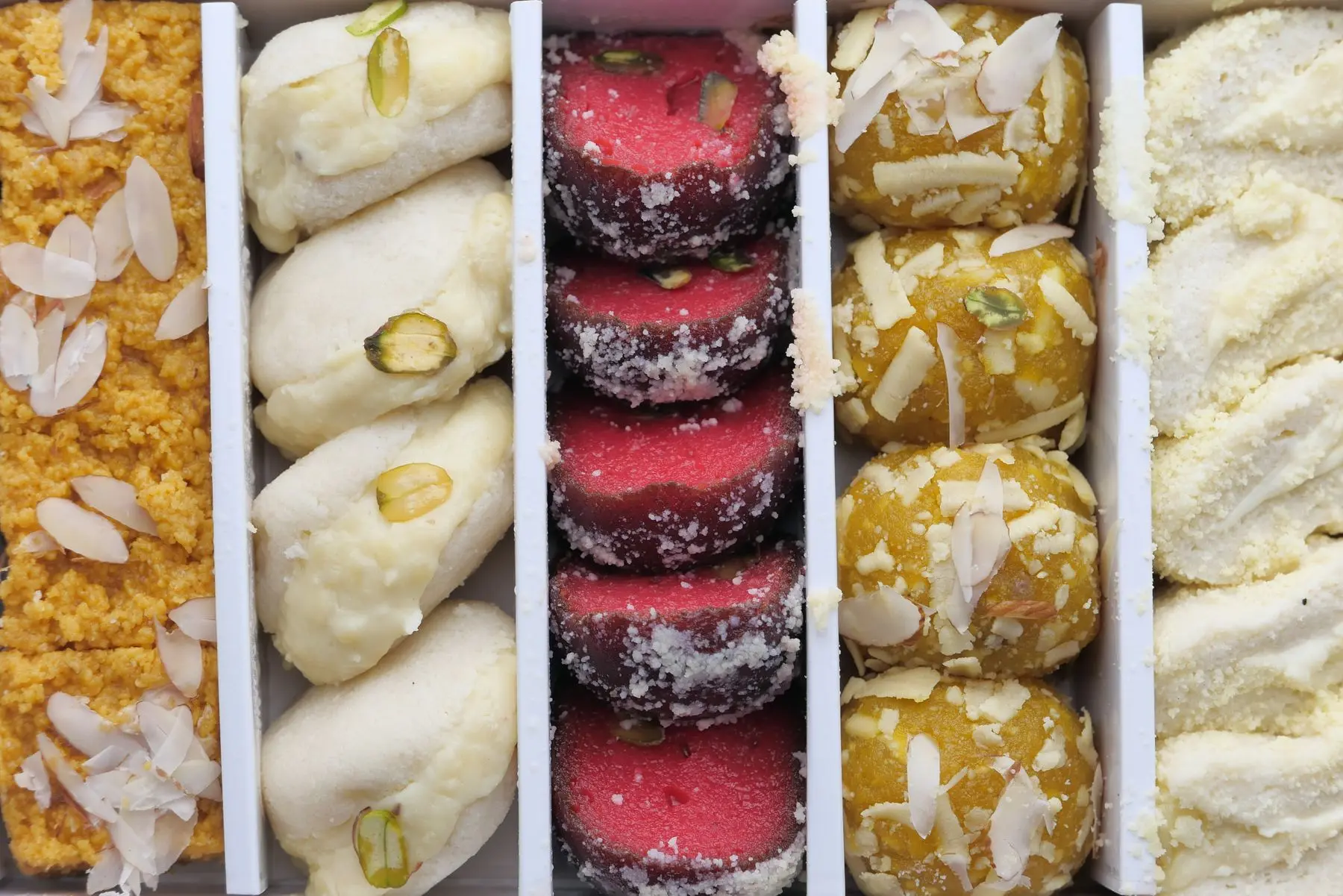 A box of white, pink and golden sandesh pressed into moulds, with pistachio slivers.
