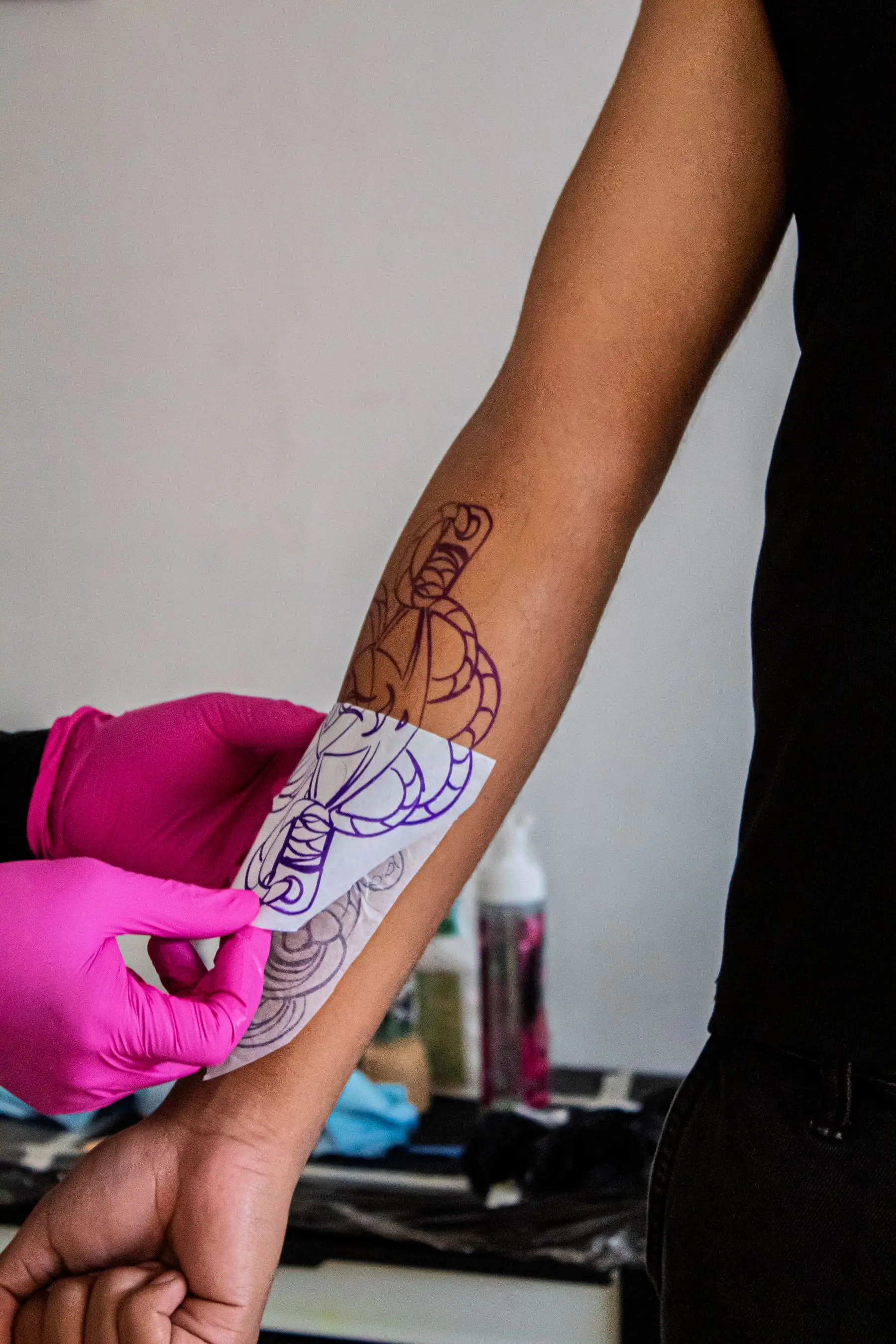 Pink-gloved hands press a butterfly stencil onto a forearm.