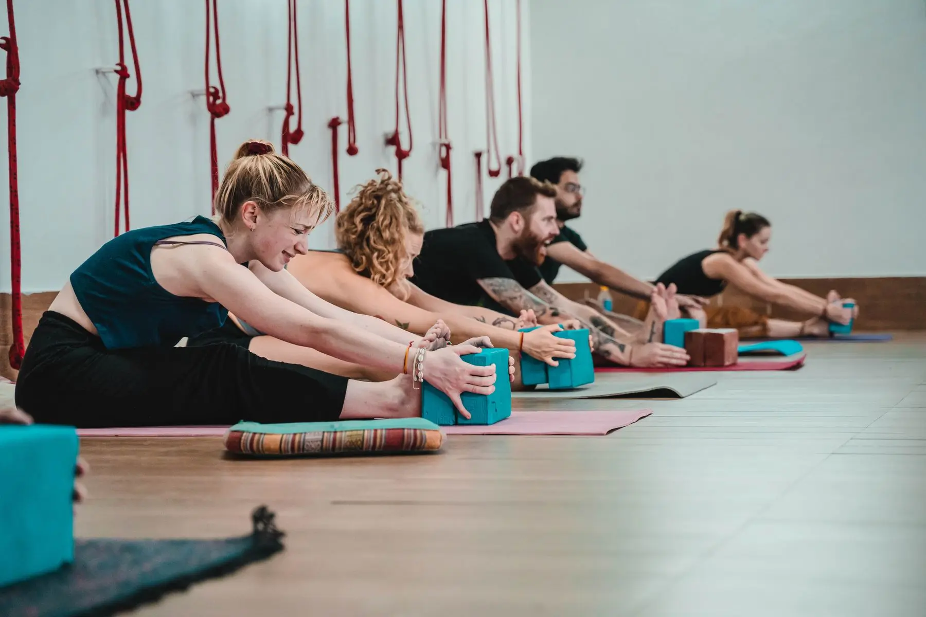 A row of people fold forward over blocks on their mats in a studio.