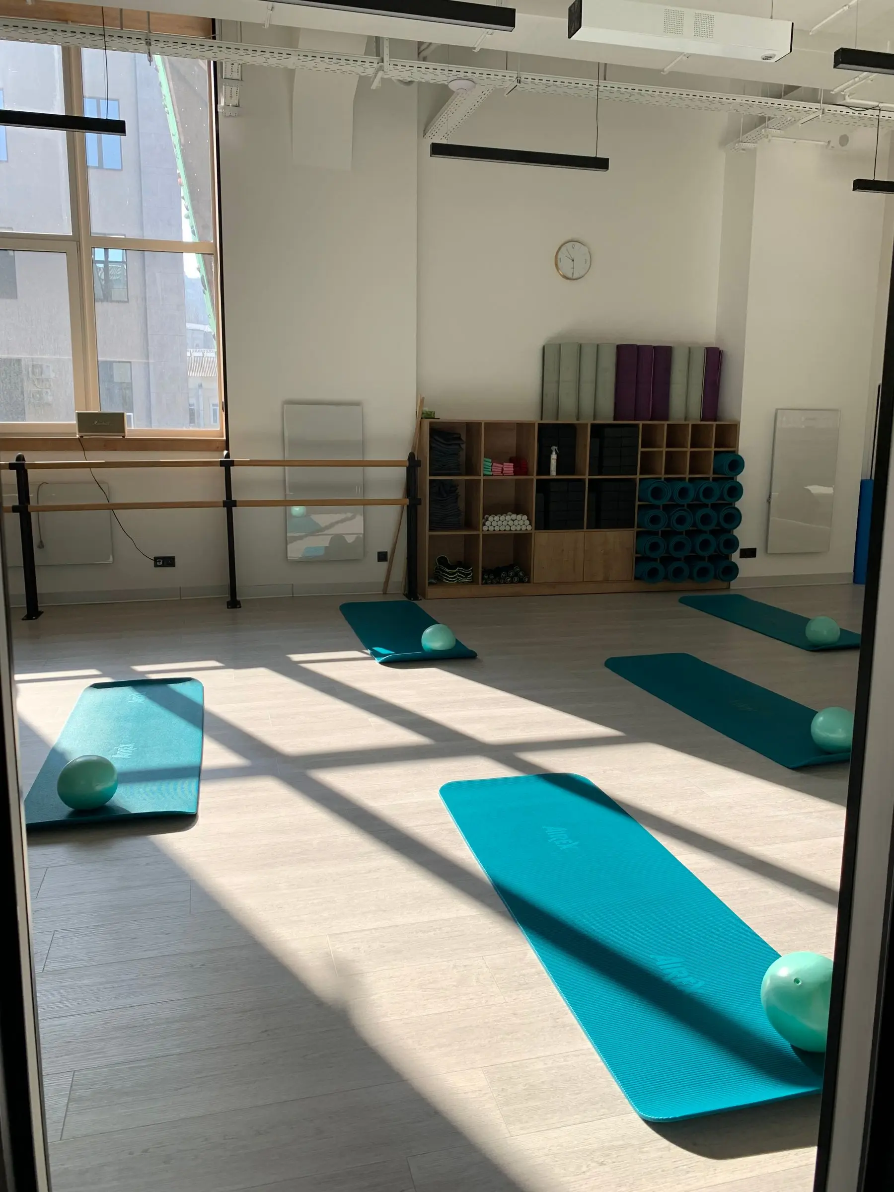 A sunlit studio floor with teal mats and soft balls beside wooden shelves.