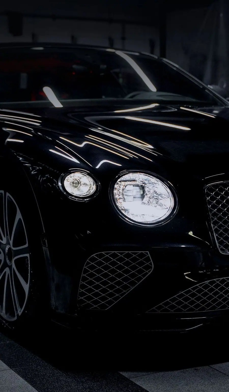 A black grand tourer in a dark bay, its headlamps lit