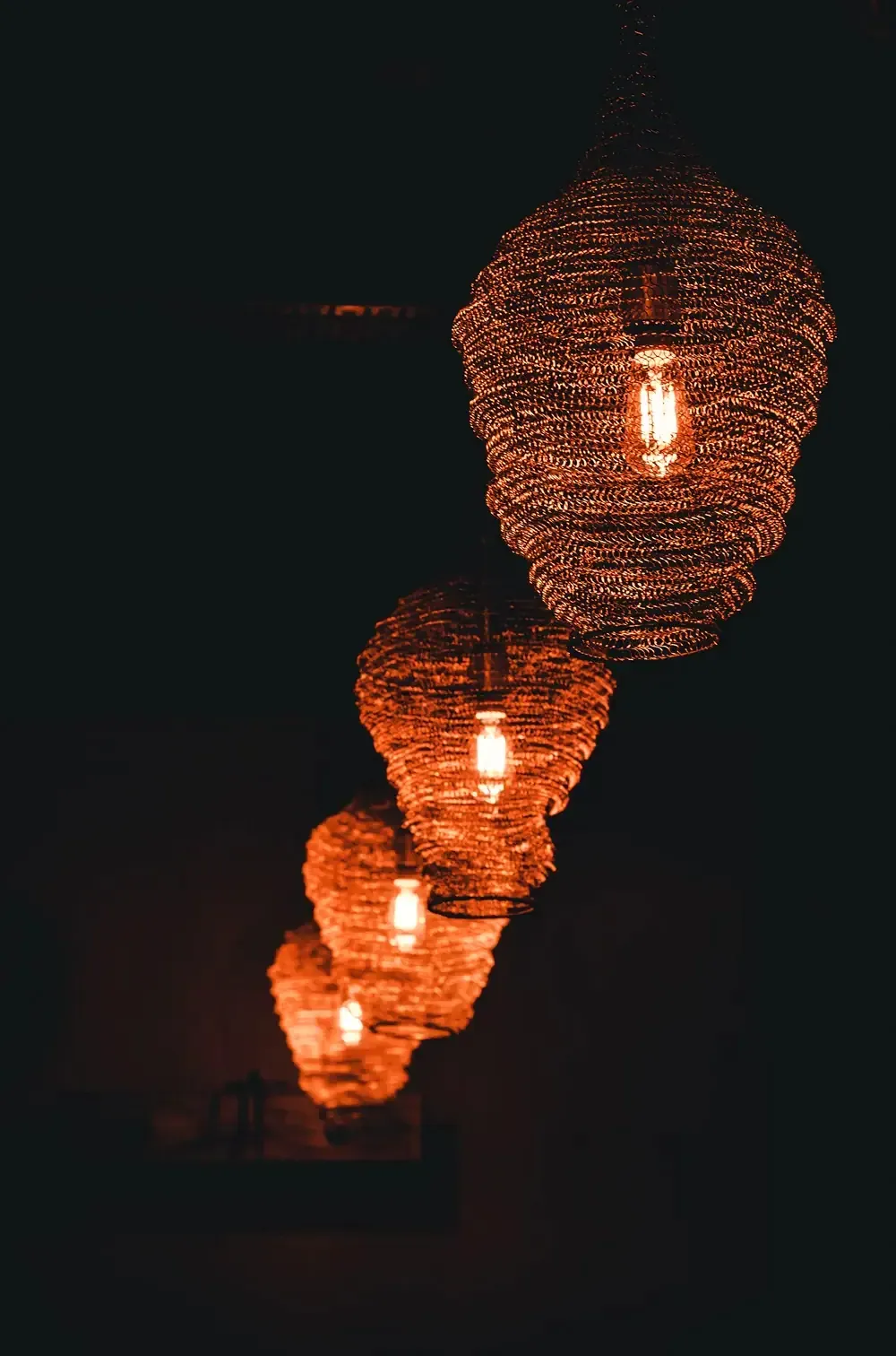 Woven wire pendant lamps glowing orange in a row