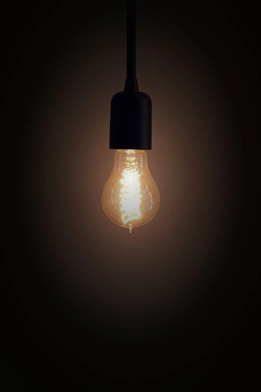 A single bare-bulb pendant lamp on a black cord, glowing in a dark room