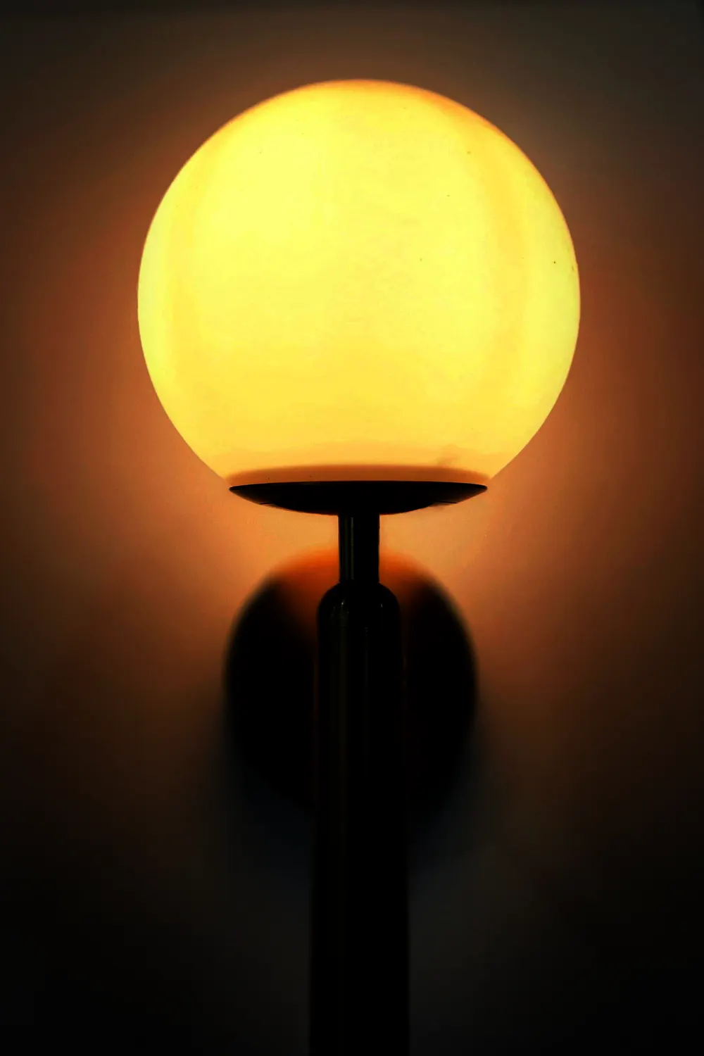 A wall sconce with an opal globe on a brass stem, glowing amber against a dark wall