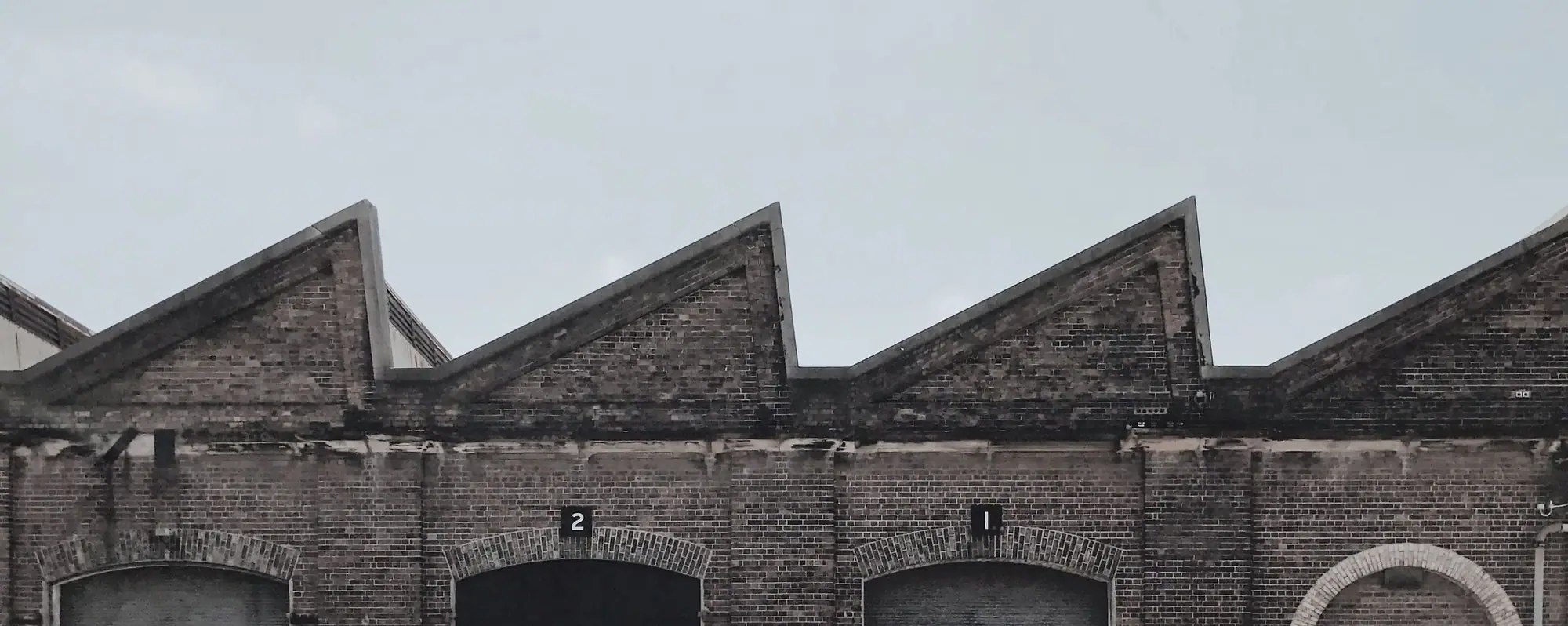A brick mill with a sawtooth roof under a pale sky