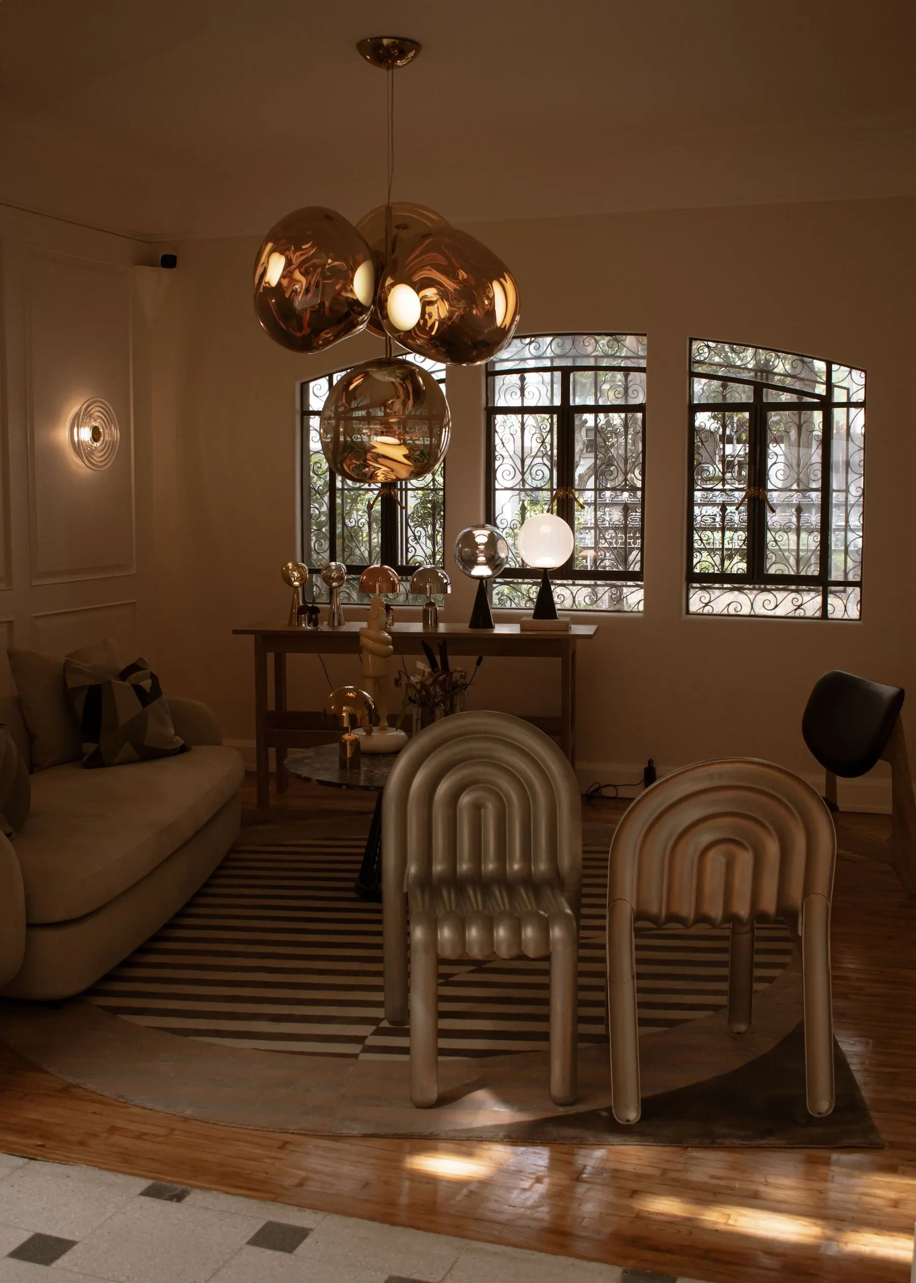 A showroom corner in warm light: copper glass pendants over a console of table lamps, a glass wall light and two sculpted chairs