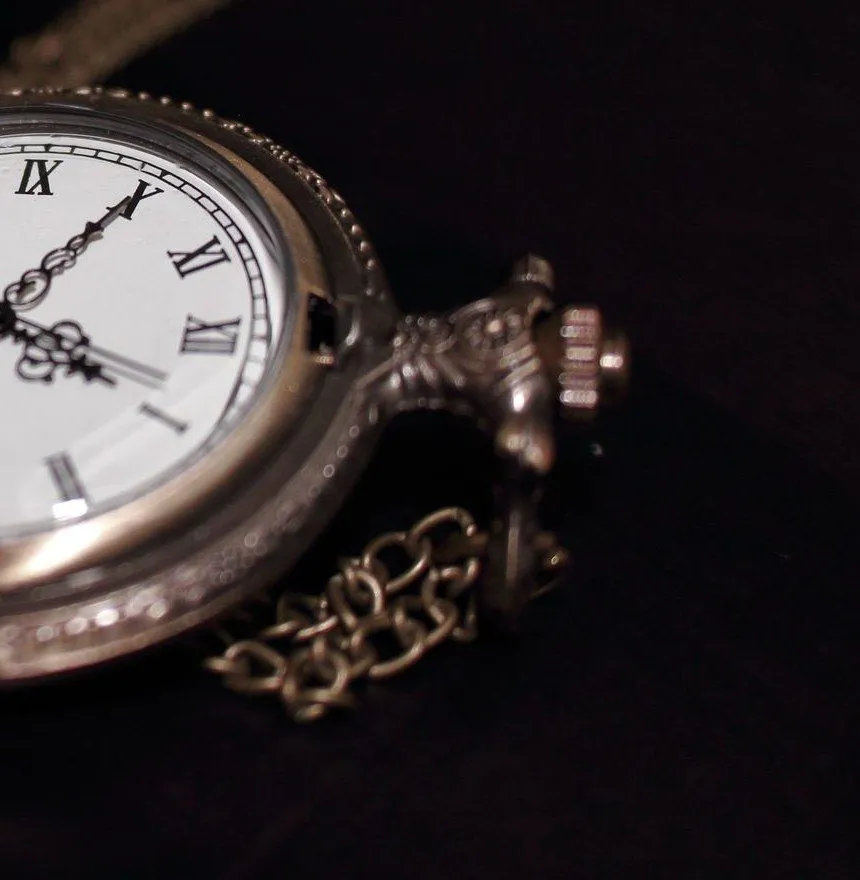 The crown, case and chain of a bronze pocket watch, lit from one side against black
