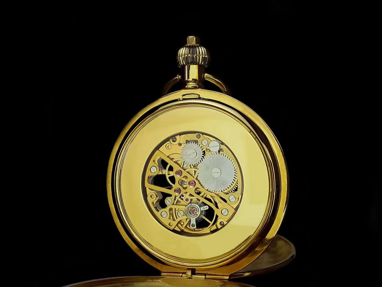 A gold pocket watch standing on black, with its back open to show the gold movement