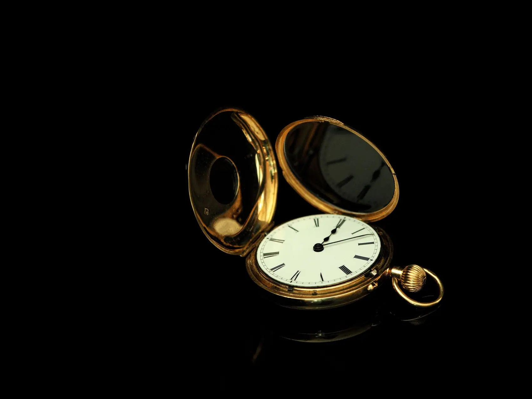 A gold hunter pocket watch open on a black reflective surface