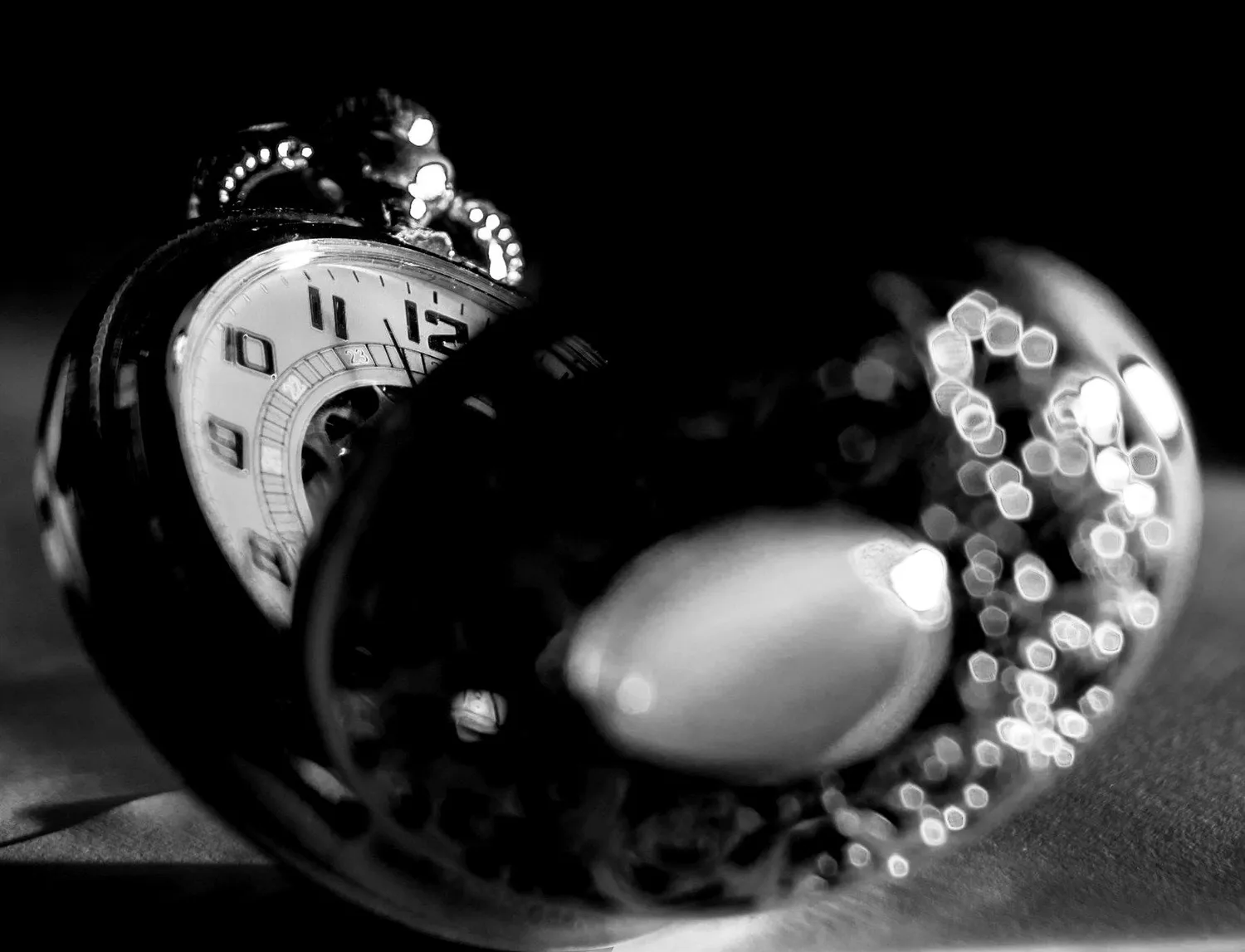 A silvered pocket watch with an engraved lid, catching one light in the dark