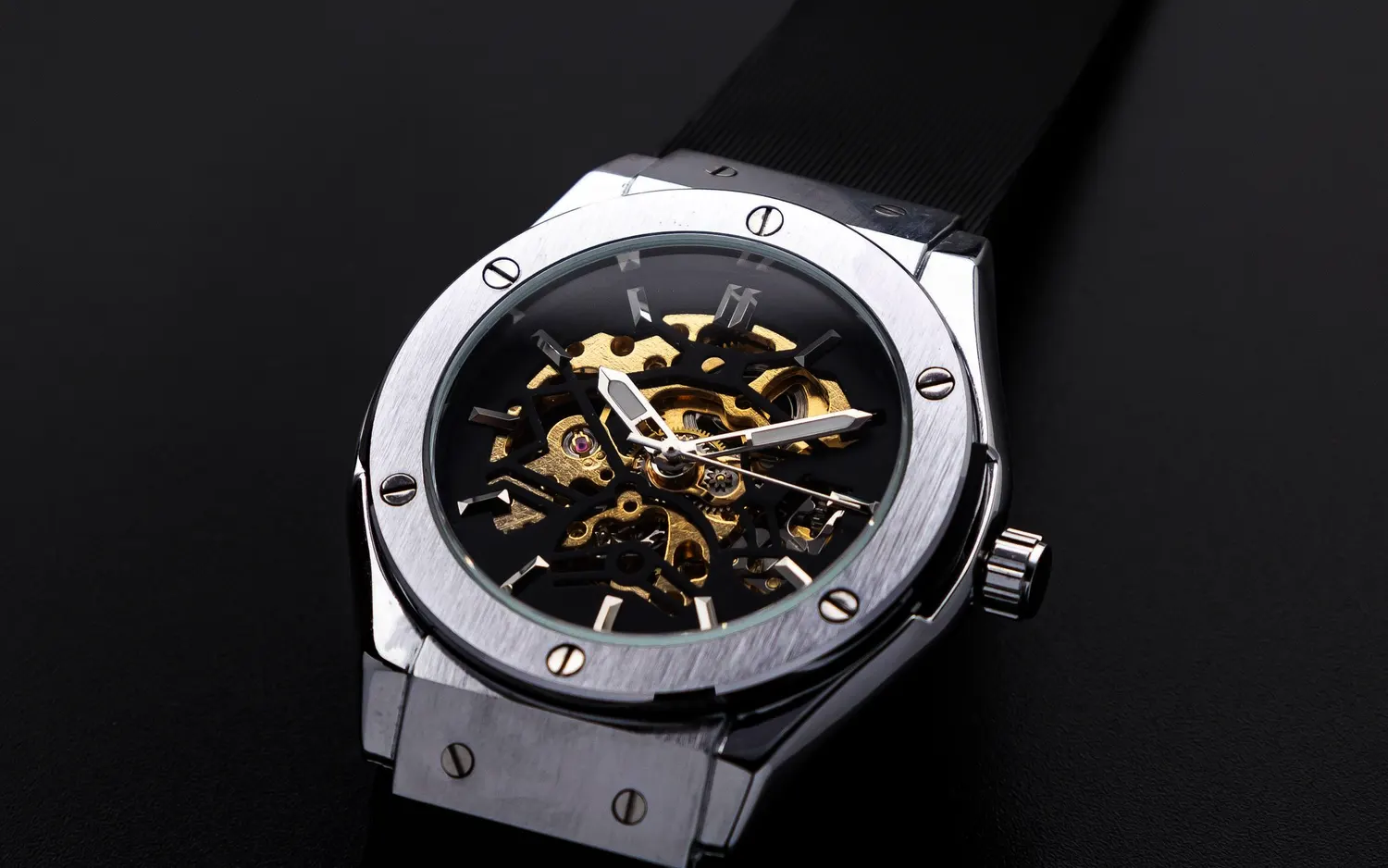 A steel wristwatch with a skeleton dial, screwed bezel and black rubber strap, on a dark surface