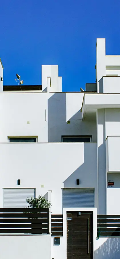 The white rendered facade of a new house with balconies, under a blue sky.