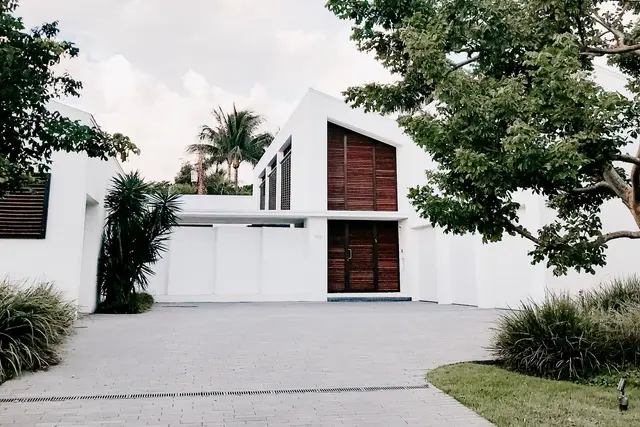 A contemporary white house with a pitched timber-clad gable and a palm tree, seen from the driveway.